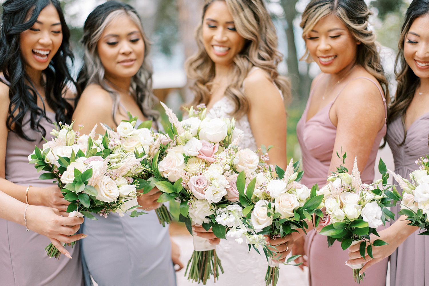 bride and bridesmaids in mismatched gowns hold pink and ivory bouquets 
