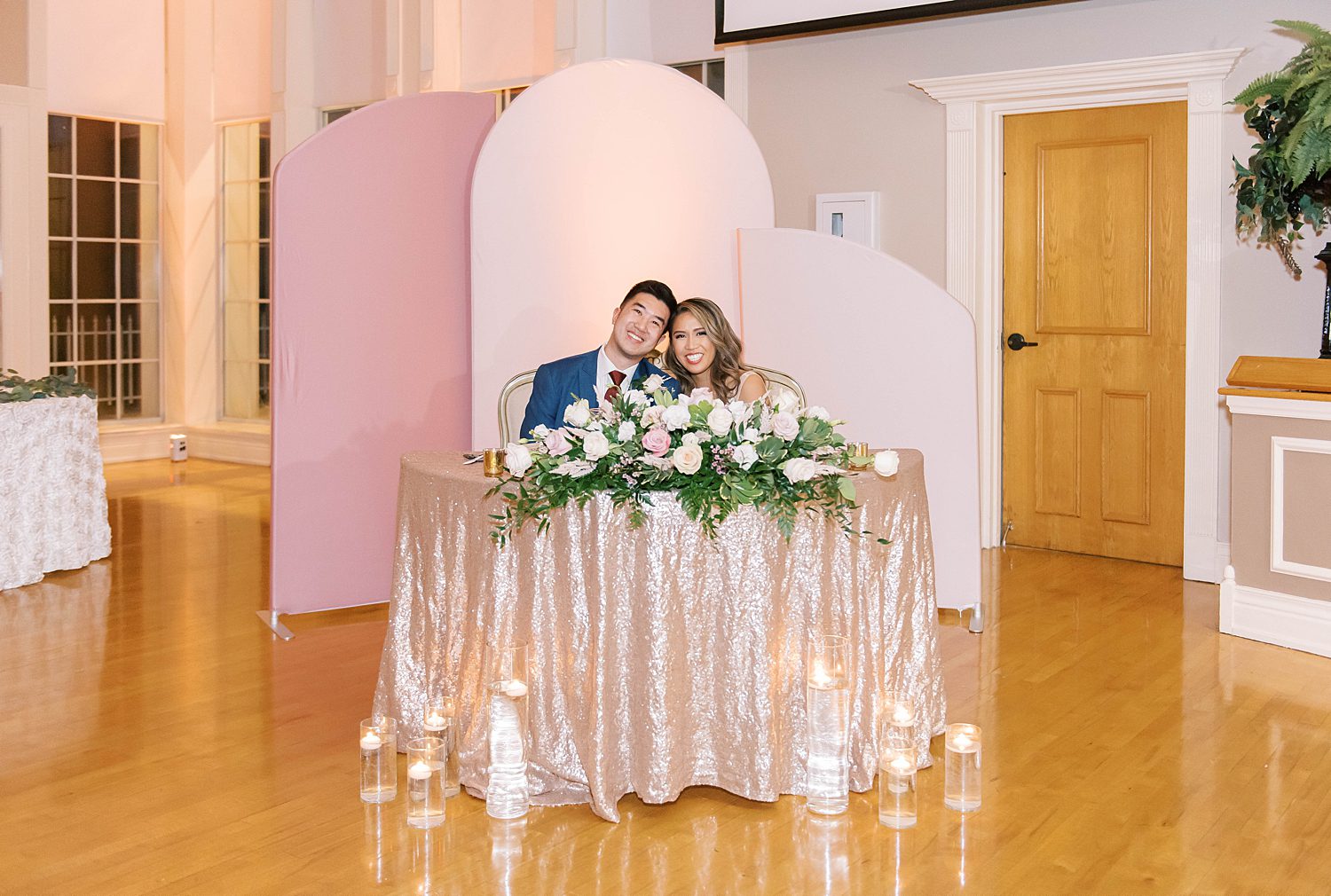 newlyweds sit at sweetheart table in front of pink displays 