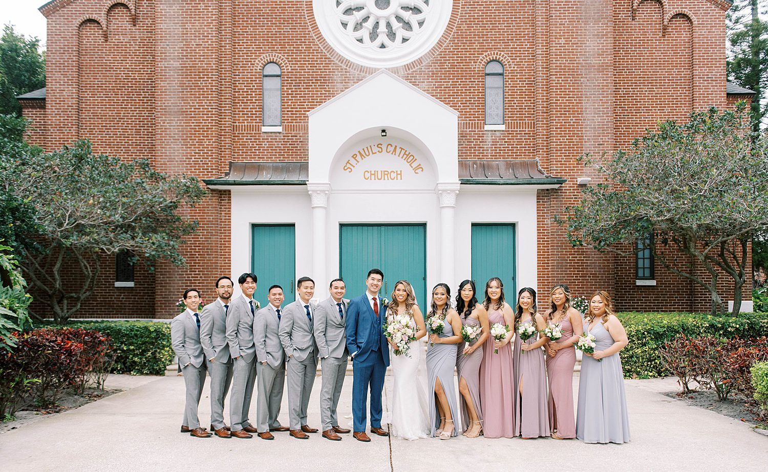 bride and groom pose in front of teal doors with wedding party at St. Paul's Catholic Church in Tampa FL