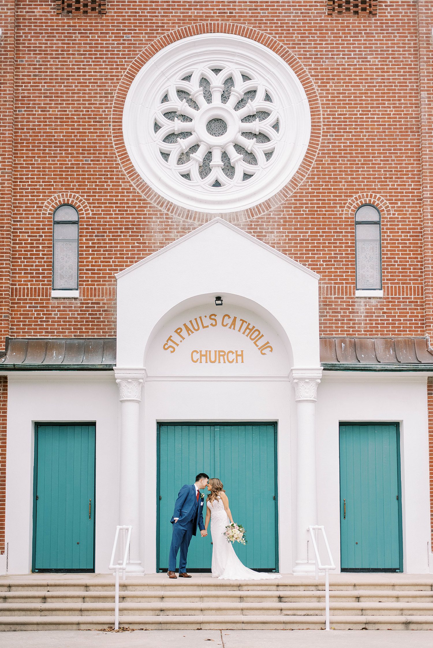bride and groom kiss in front of teal doors in front of St. Paul's Catholic Church in Tampa FL