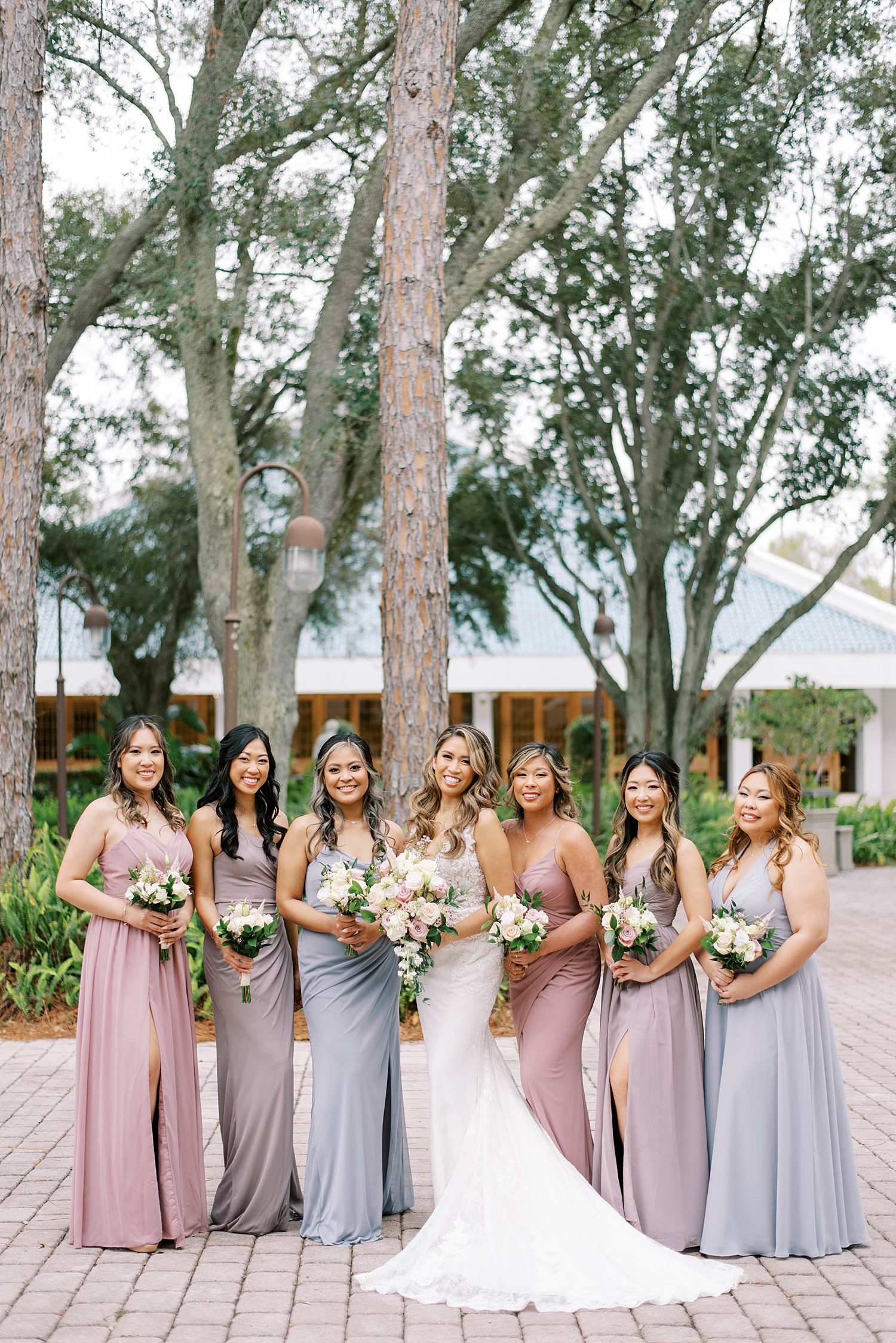bride poses with bridesmaids in mismatched purple and blue gowns 