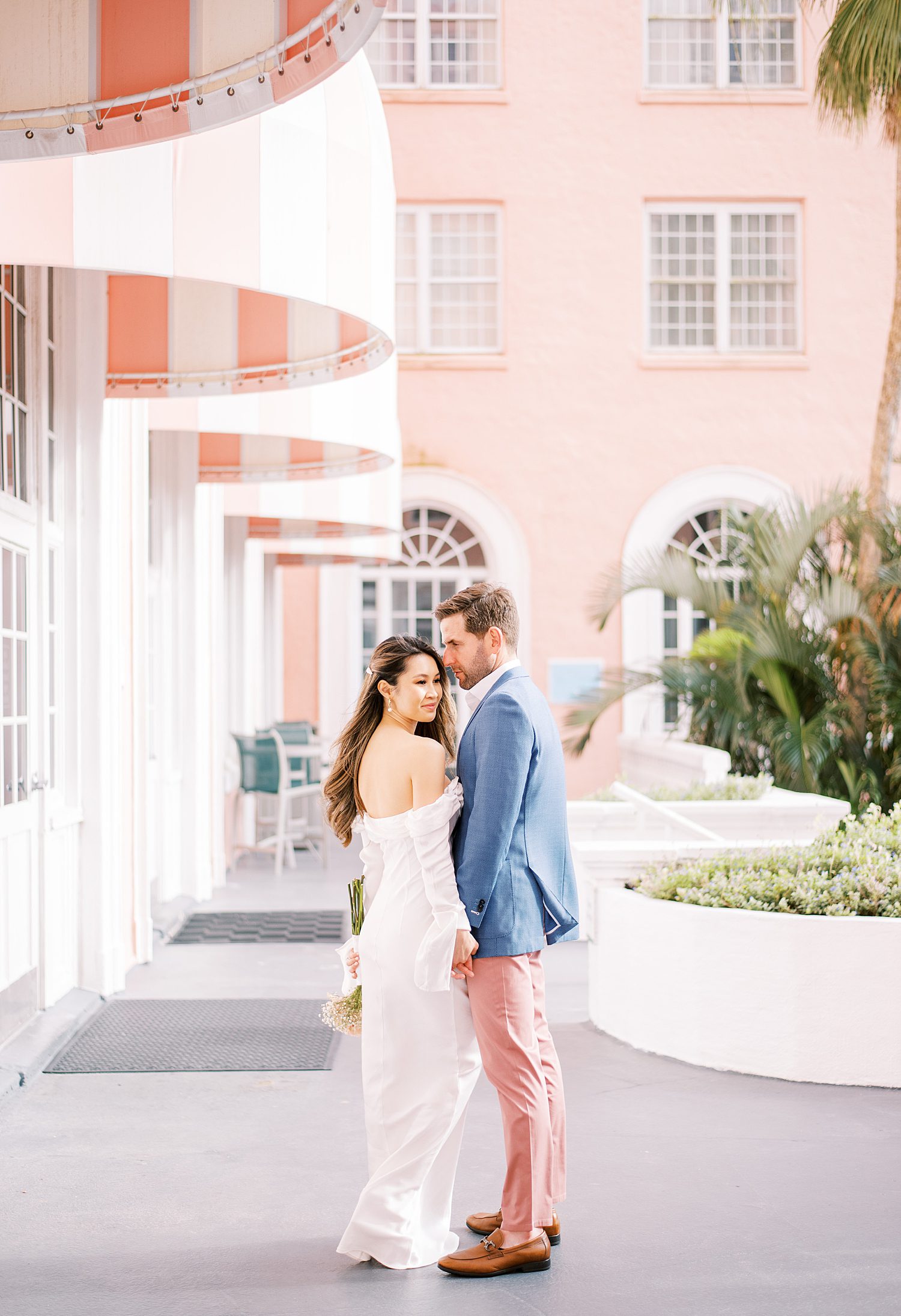 groom in blue jacket and pink pants hugs fiancee to him