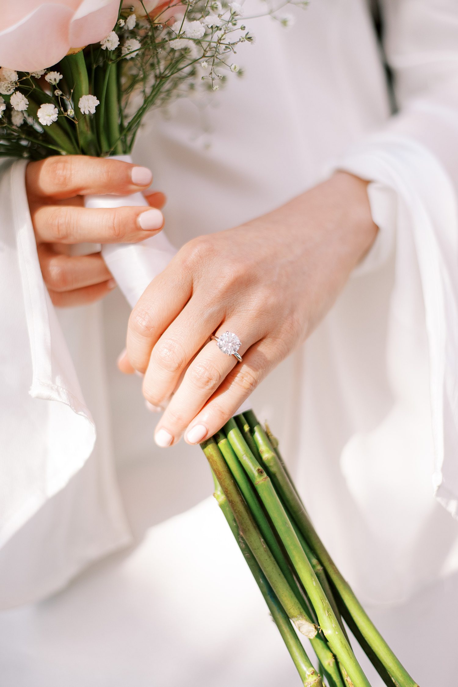 woman holds stems on small bouquet showing off diamond ring 