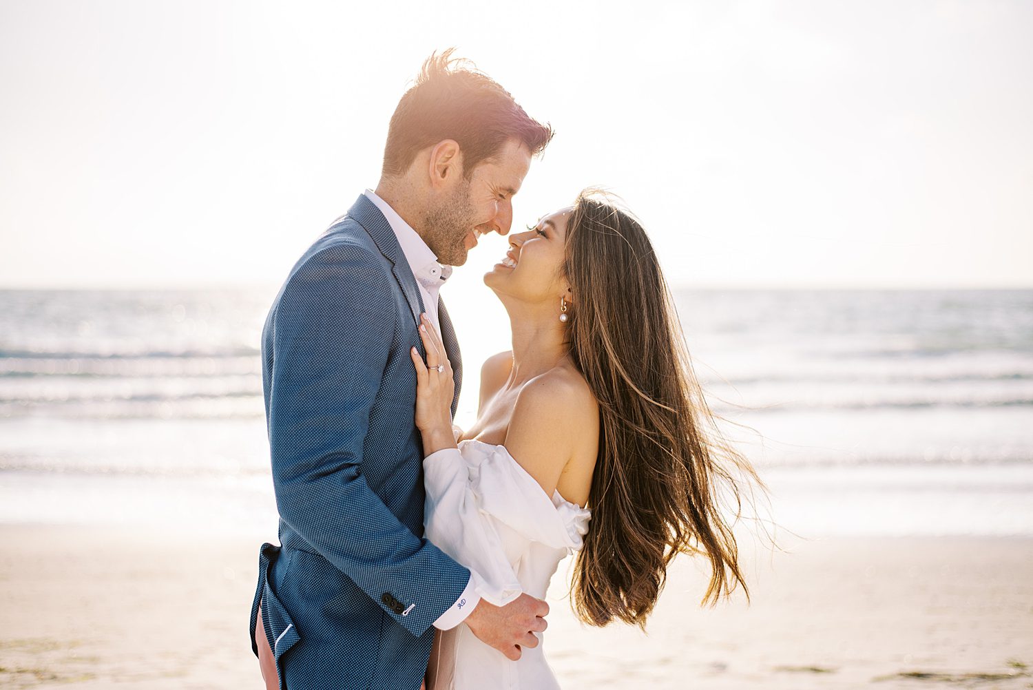 engaged couple hugs looking at each other at sunset on the beach 