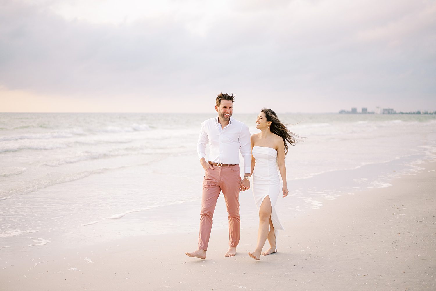 engaged couple holds hands laughing walking on St. Pete Beach
