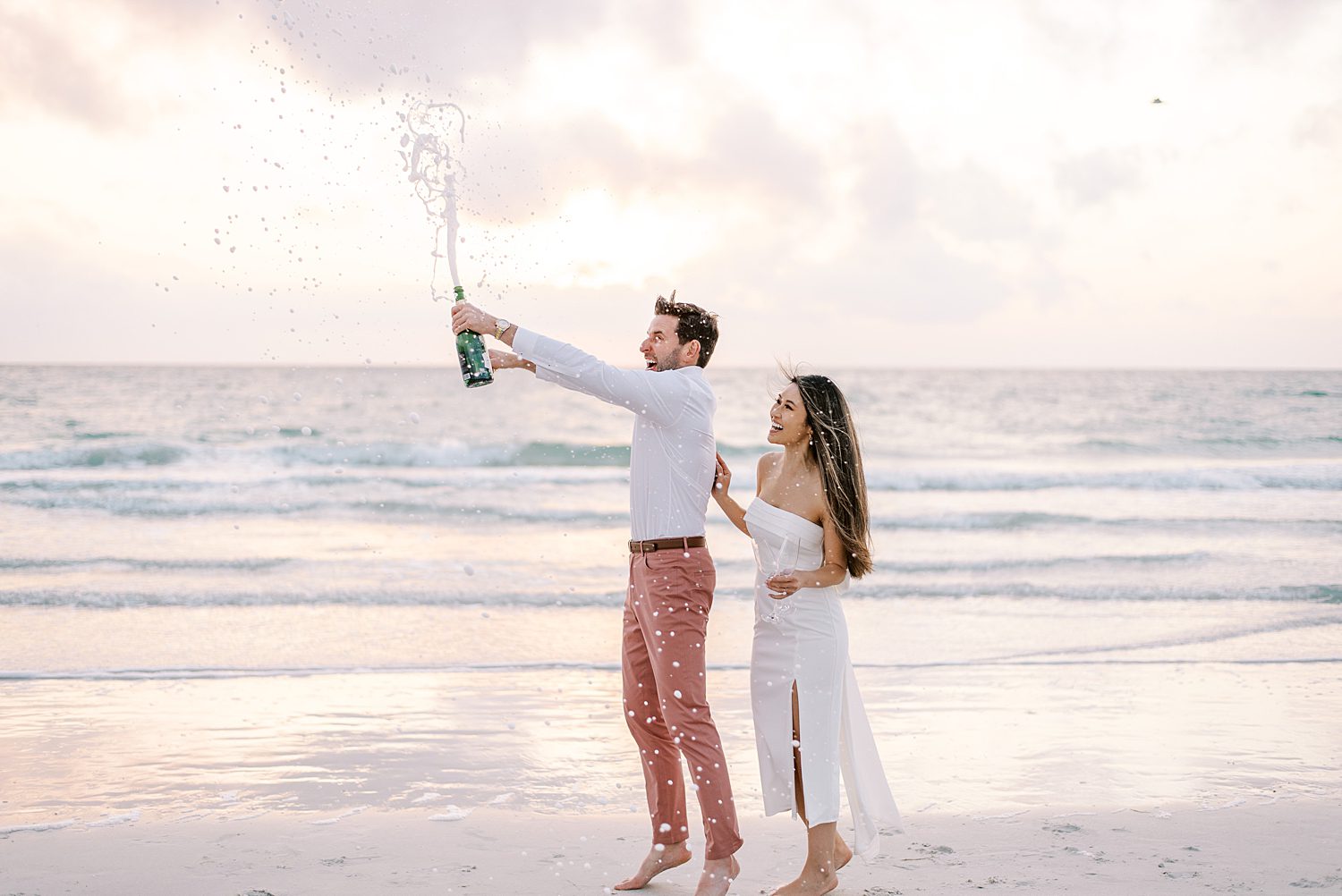 man pops champagne while bride laughs behind him on St. Pete Beach 