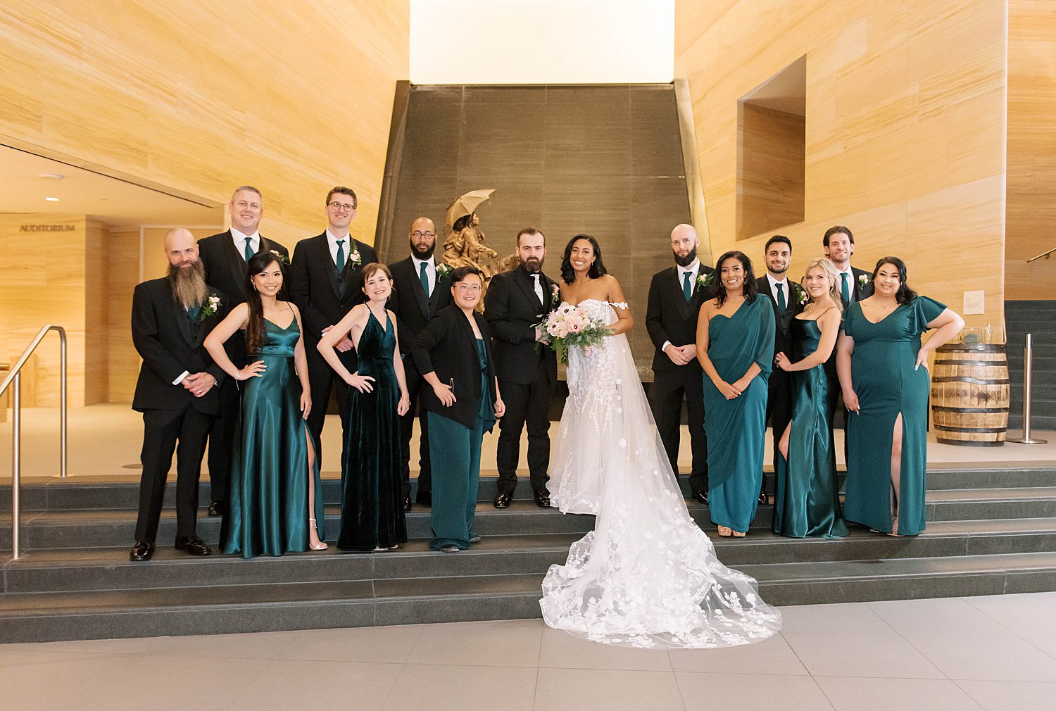 bride and groom stand on steps with wedding party in teal dresses with black suits outside The James Museum