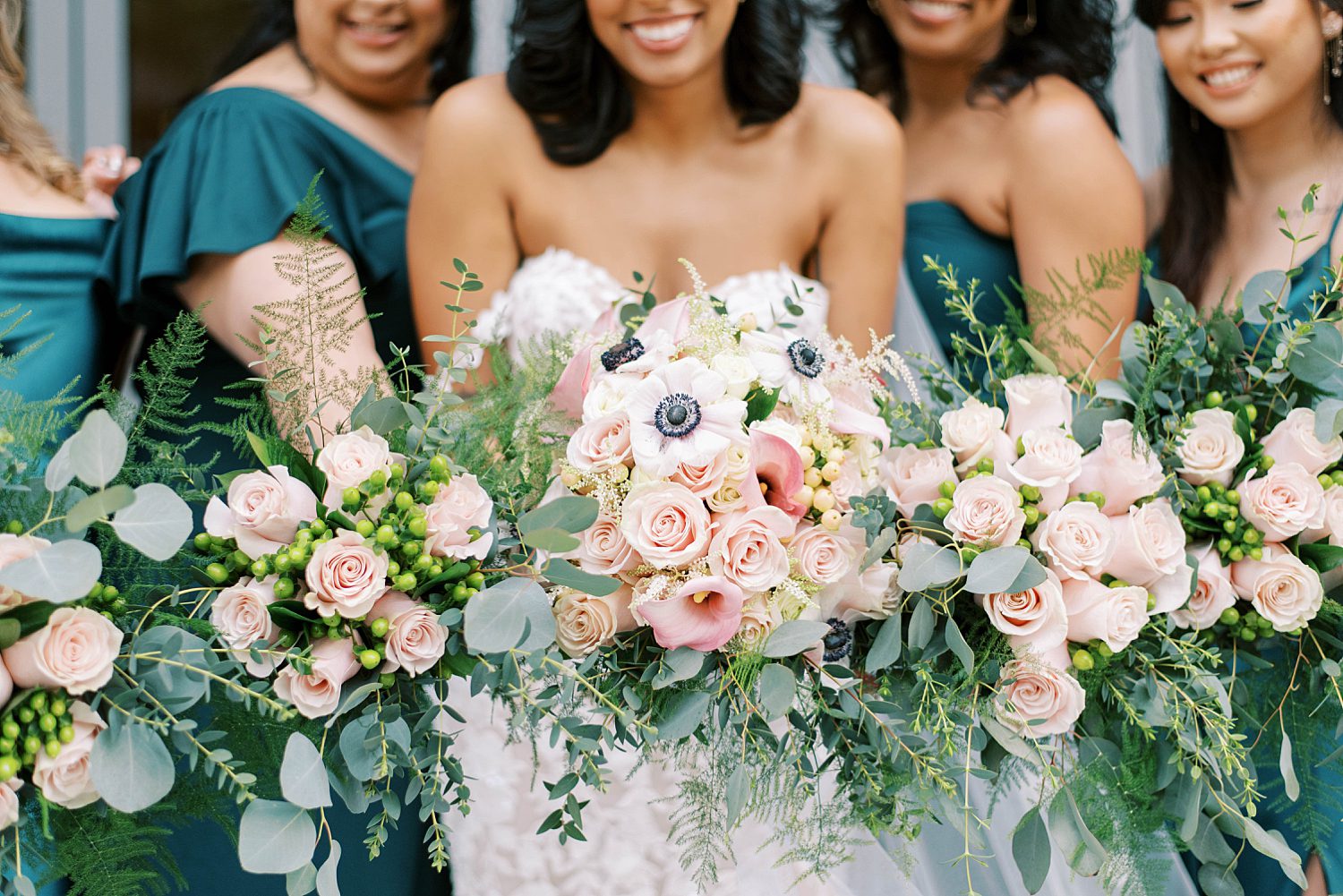 bride poses with bridesmaids in teal gowns holding pink and ivory flowers