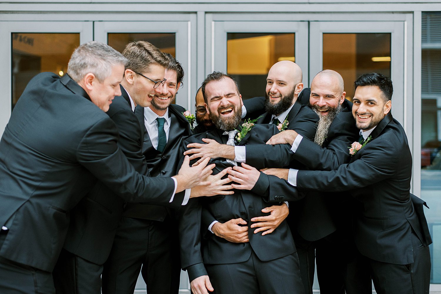 groom and groomsmen hug making funny faces outside entrance of The James Museum