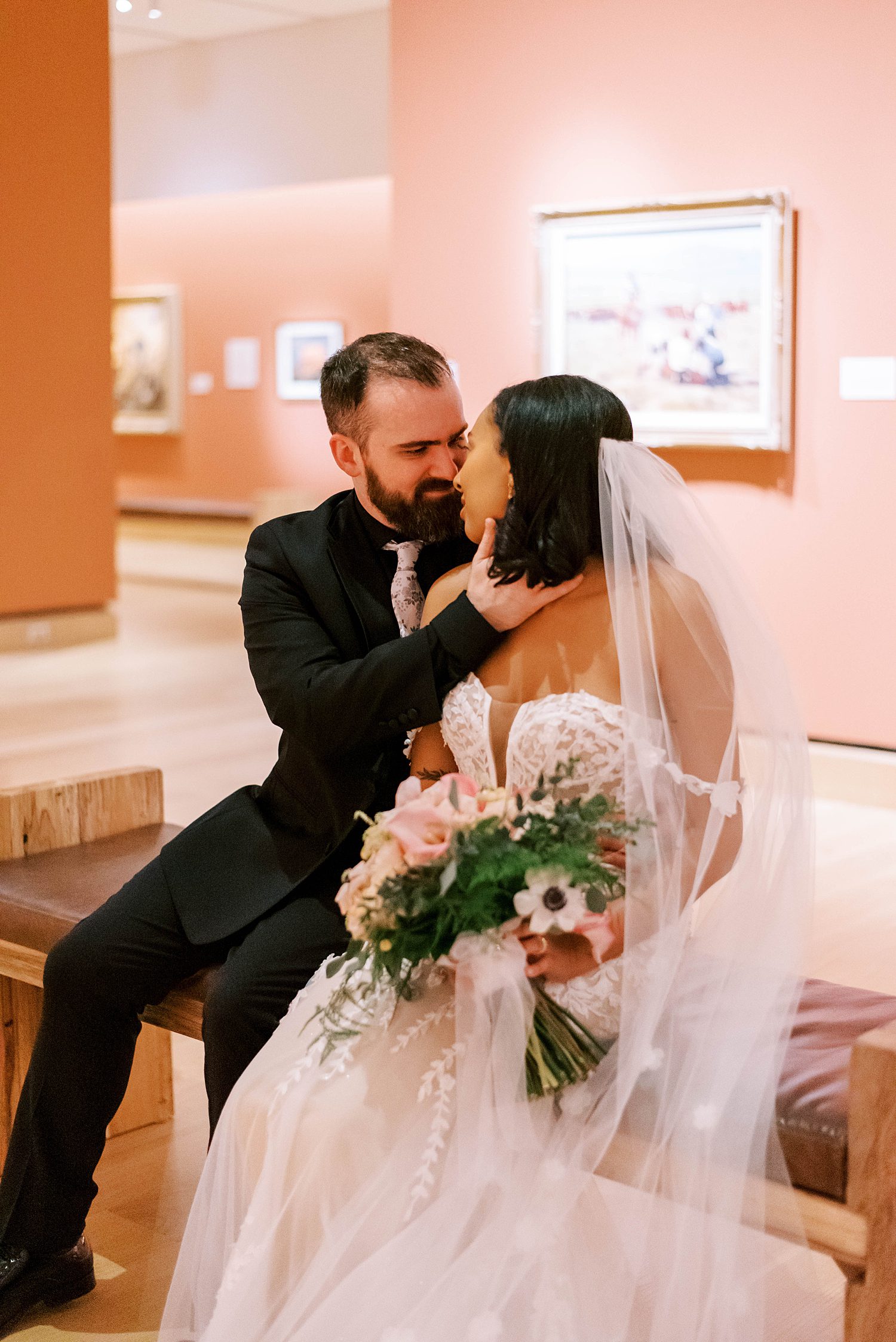 newlyweds sit on bench in gallery with pink walls at The James Museum