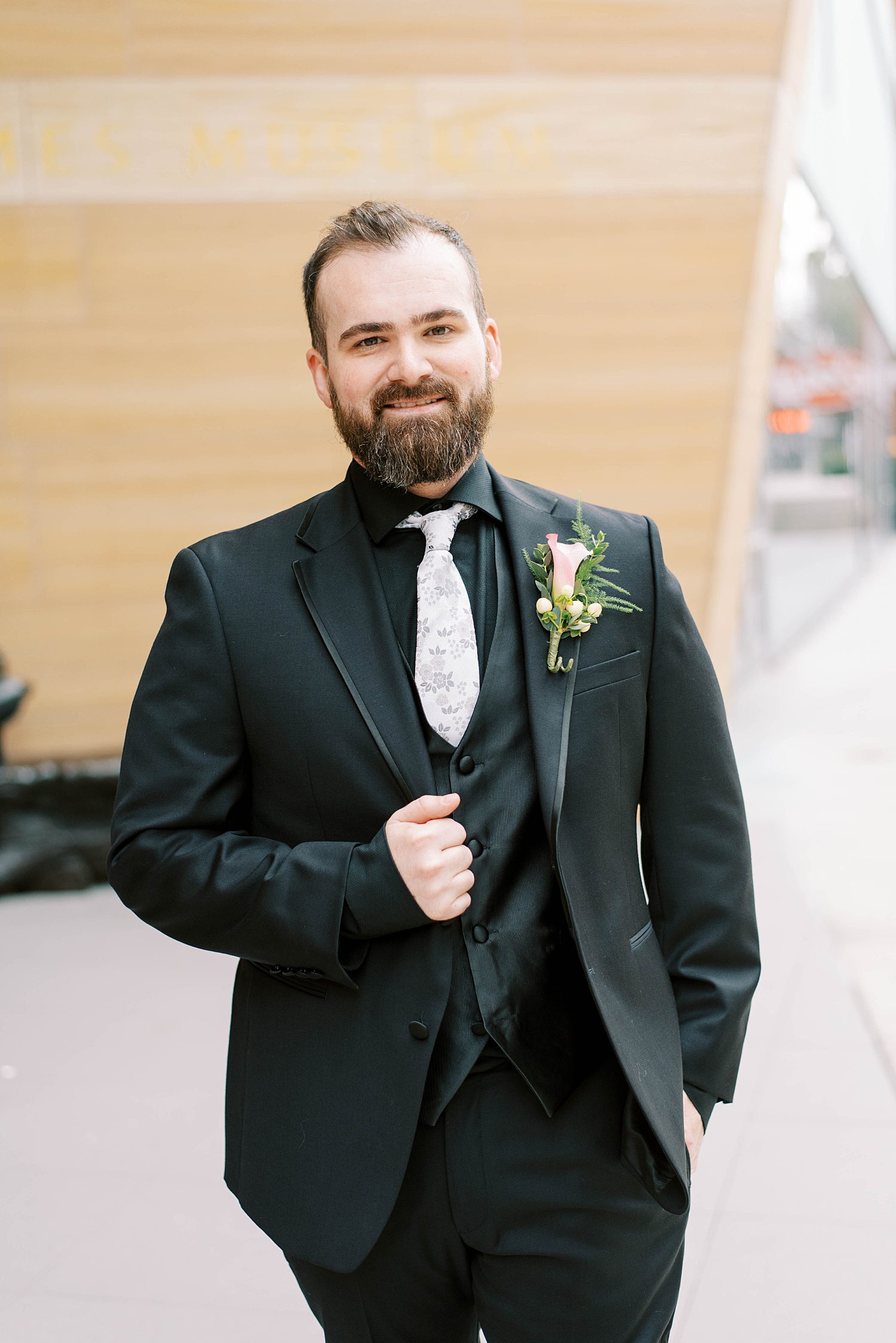 groom stands outside The James Museum in black suit with white tie
