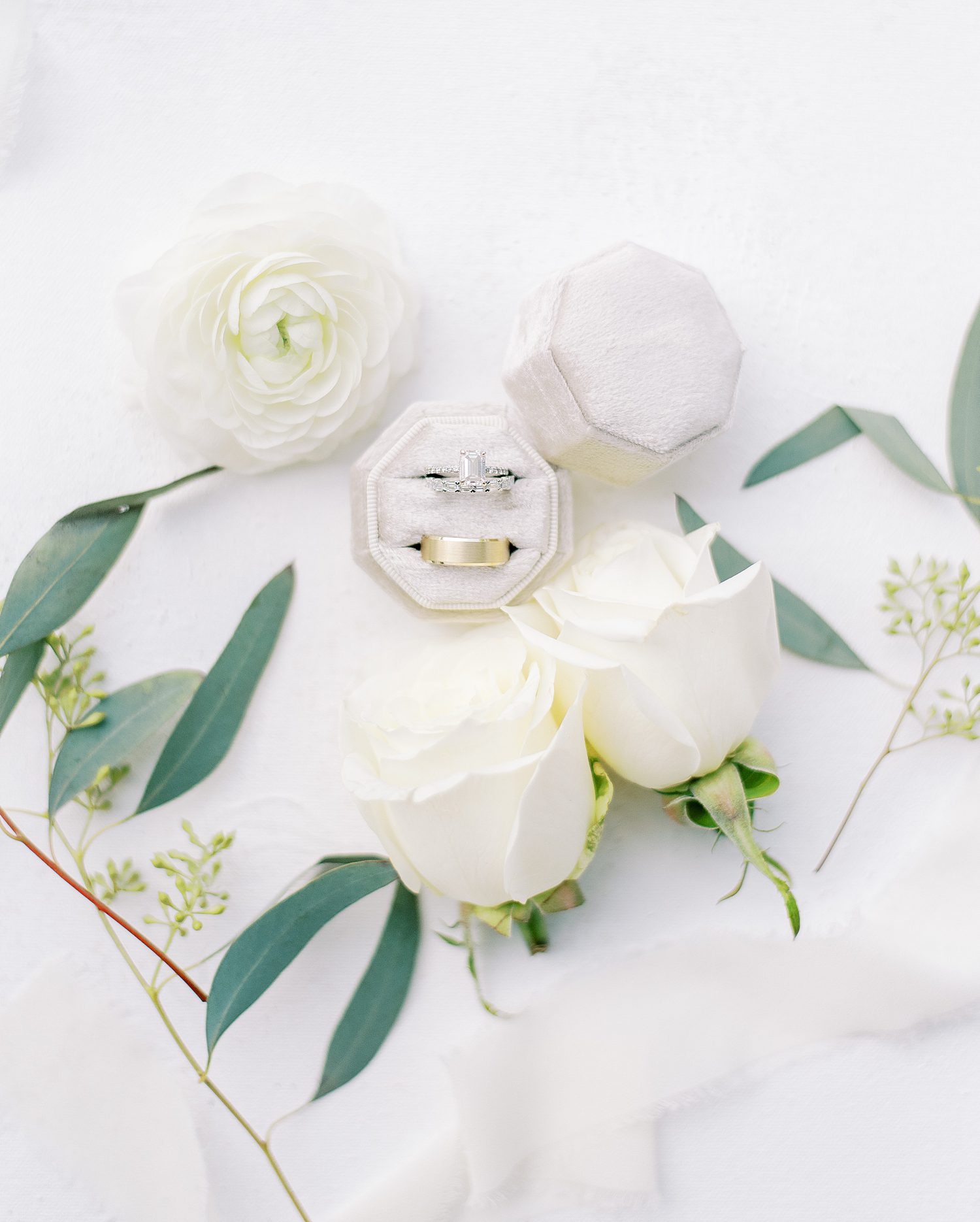 white roses surround silver wedding bands in white ring boxes