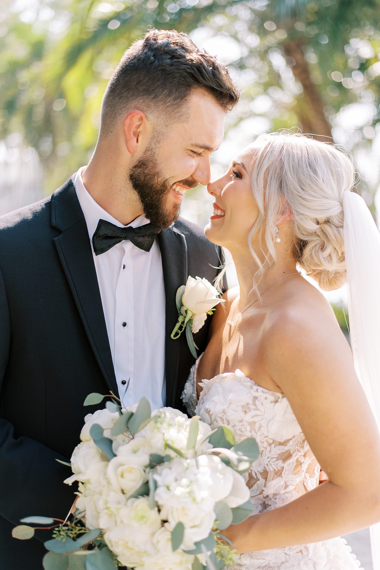 bride and groom smile together touching noses while bride holds ivory bouquet