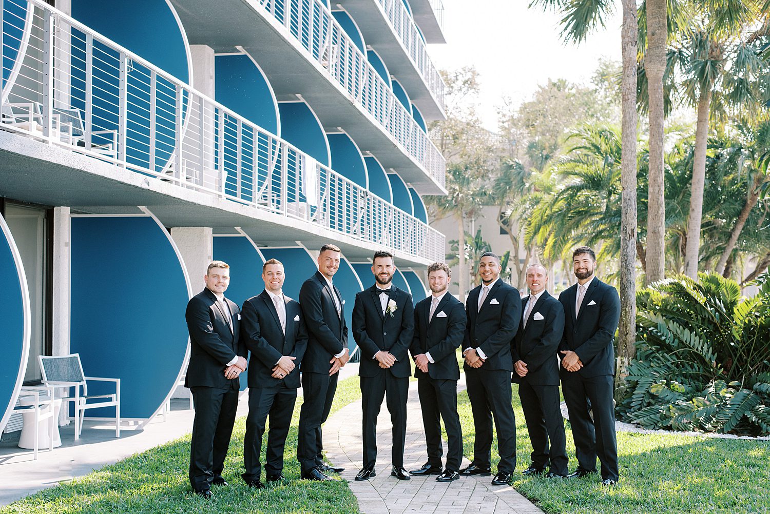 groom stands with groomsmen in front of blue balconies at The Godfrey