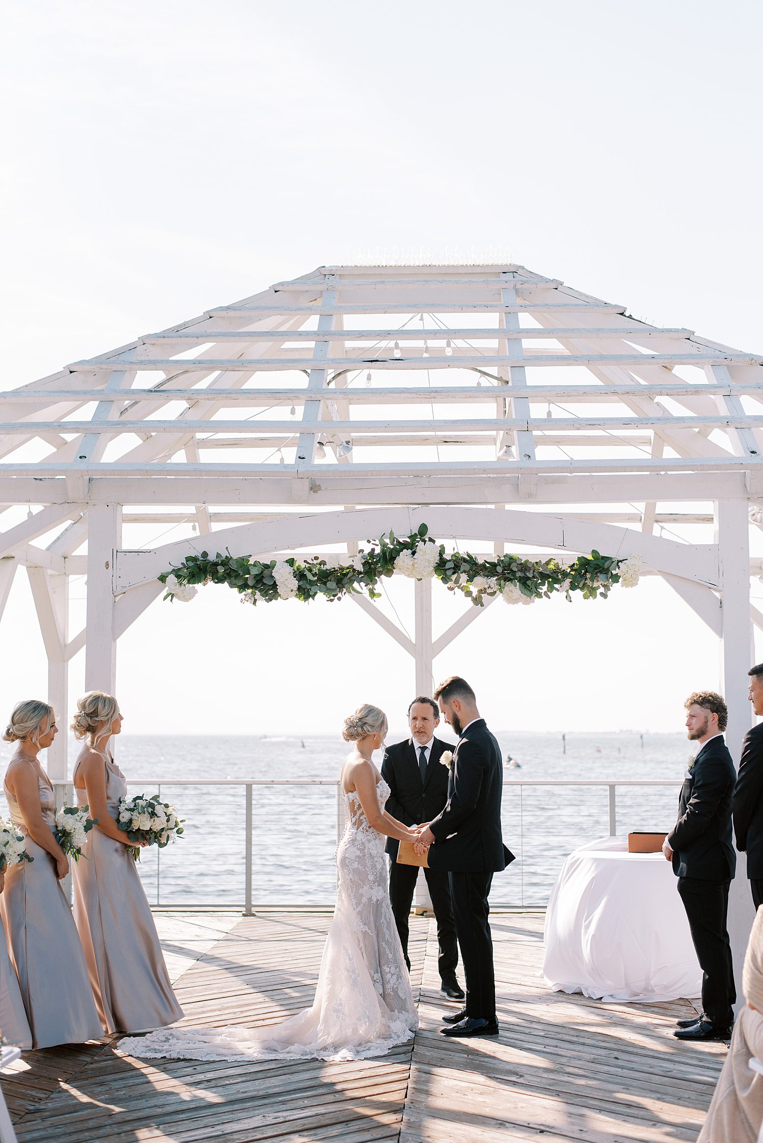 bride and groom stand under white gazebo during waterfront ceremony at The Godfrey