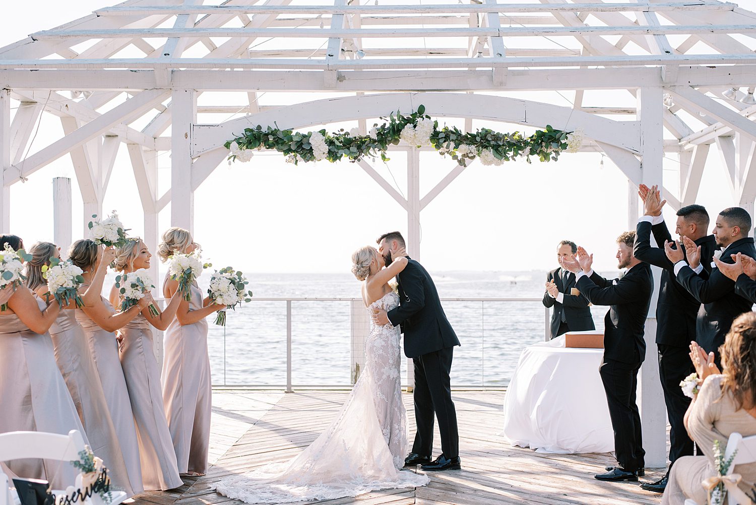 newlyweds kiss under white arbor during The Godfrey wedding ceremony
