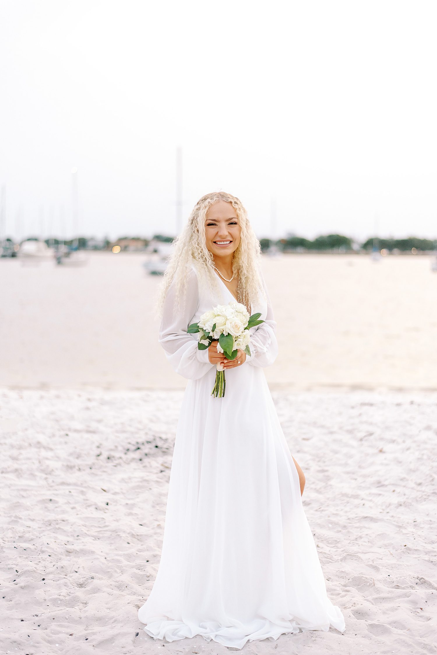 bride stands on beach holding small ivory bouquet 