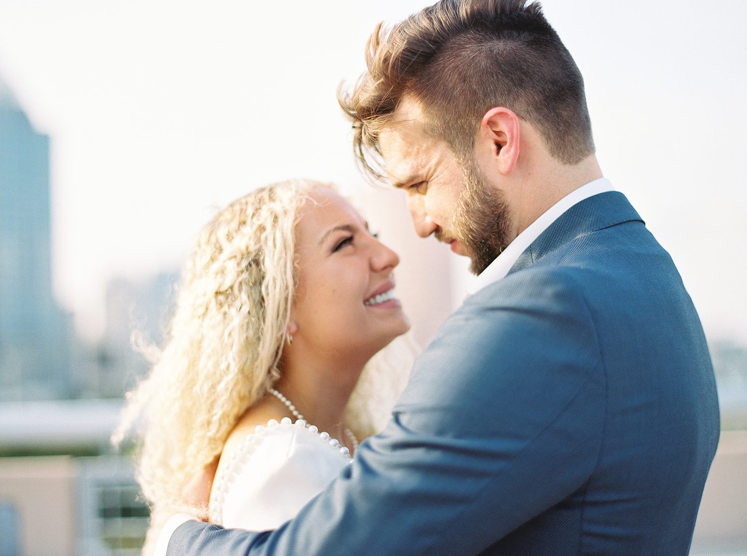 woman in white dress with pearl accents smiles up at man in navy suit