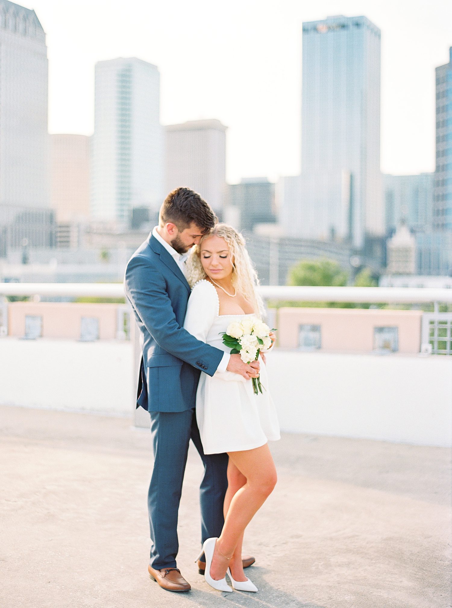 man in navy suit hugs woman in short white dress with pearl accents
