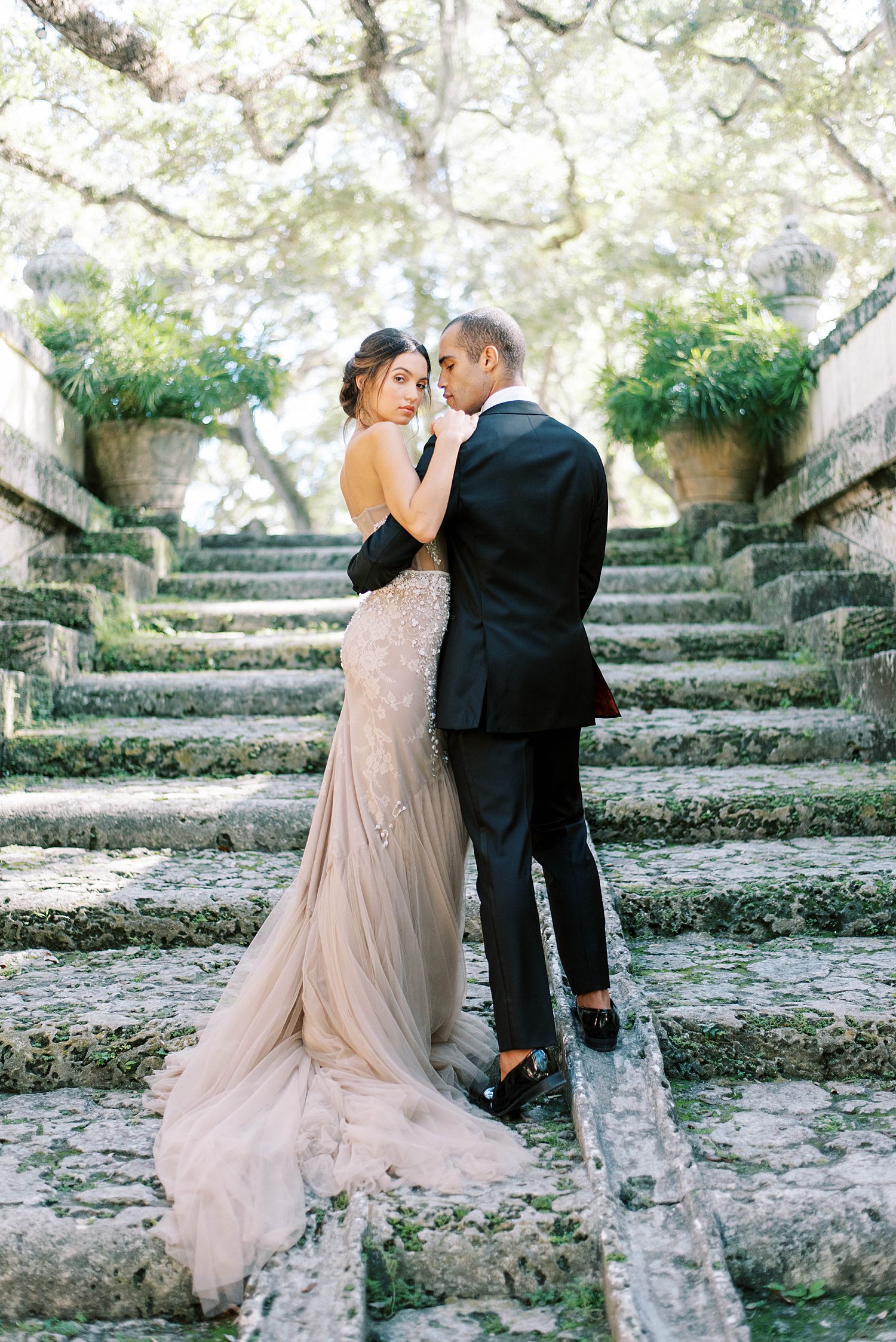bride and groom hug on steps with bride's champagne dress trailing behind her