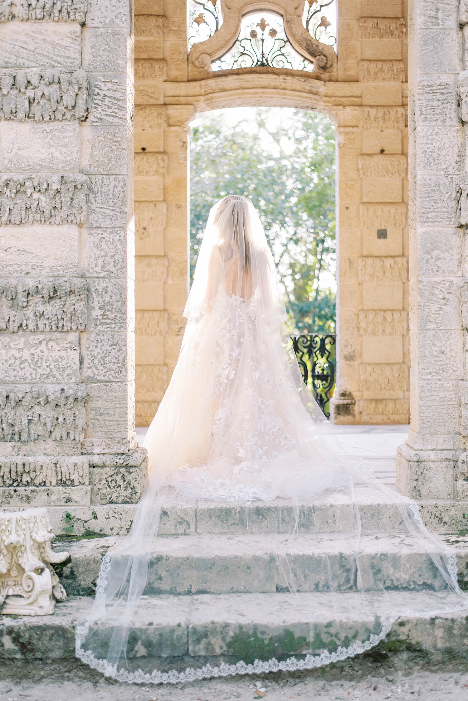 bride stands in stone arbor with veil draped behind her
