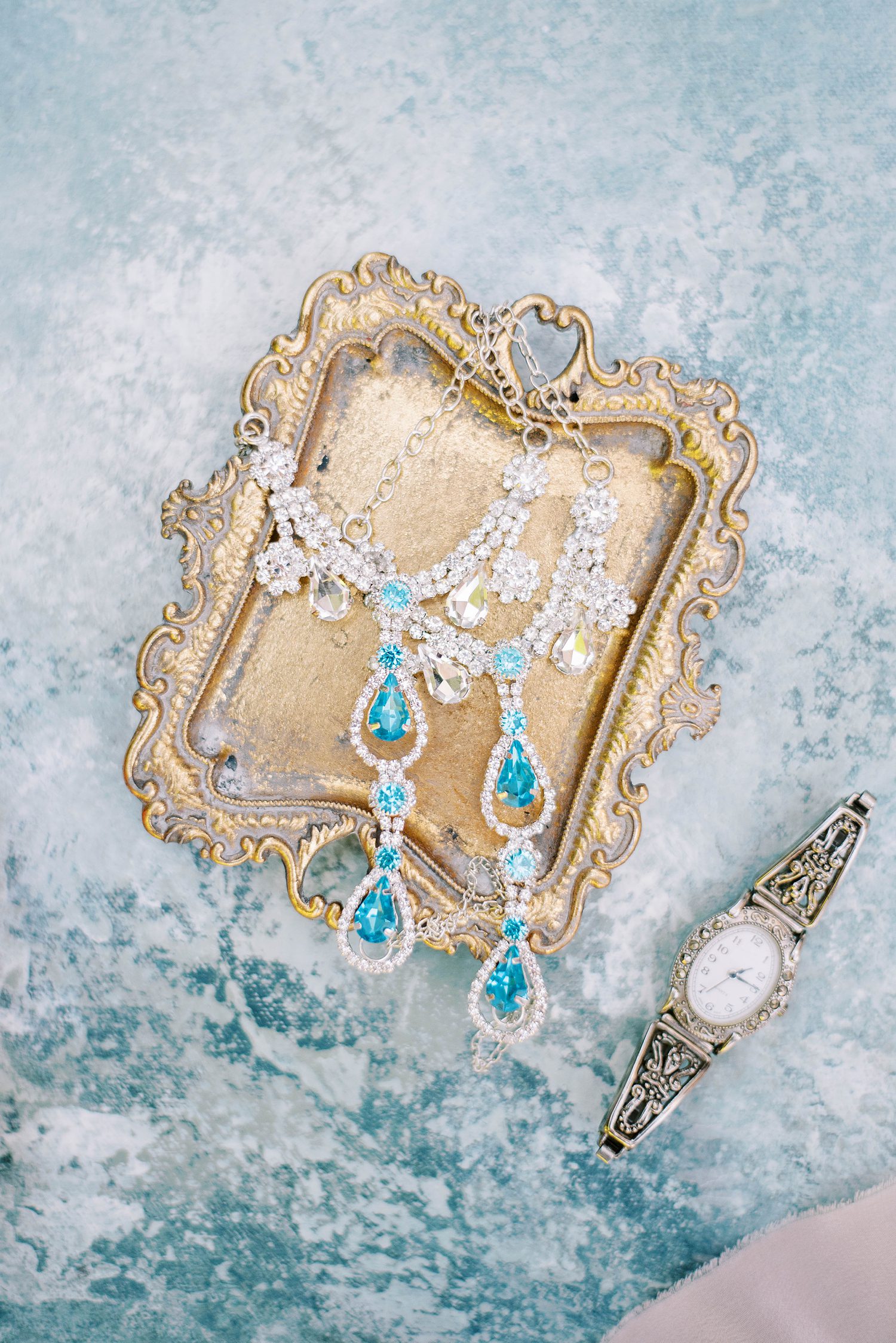 bride's blue and silver jewelry lays on gold tray