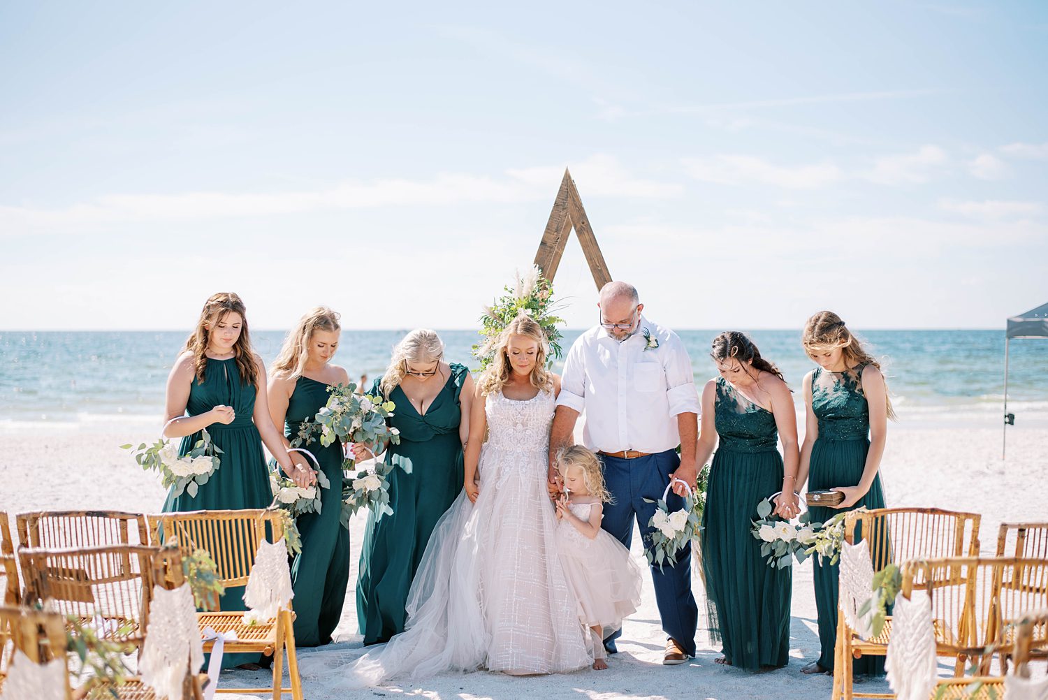 bride and groom hold hands praying with daughters after beach wedding