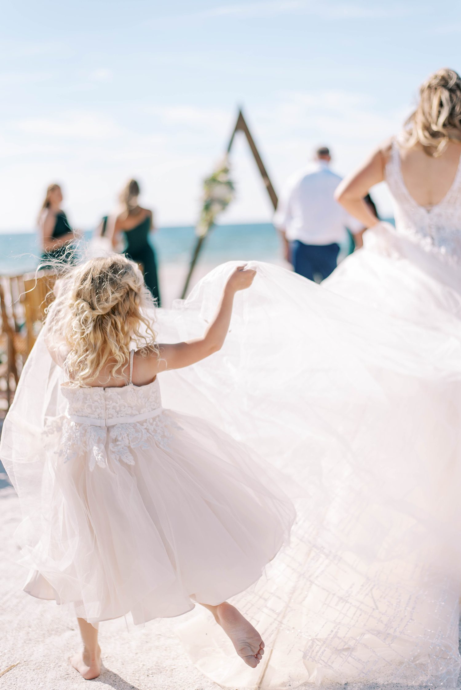 flower girl lifts up bride's wedding dress skirt on beach