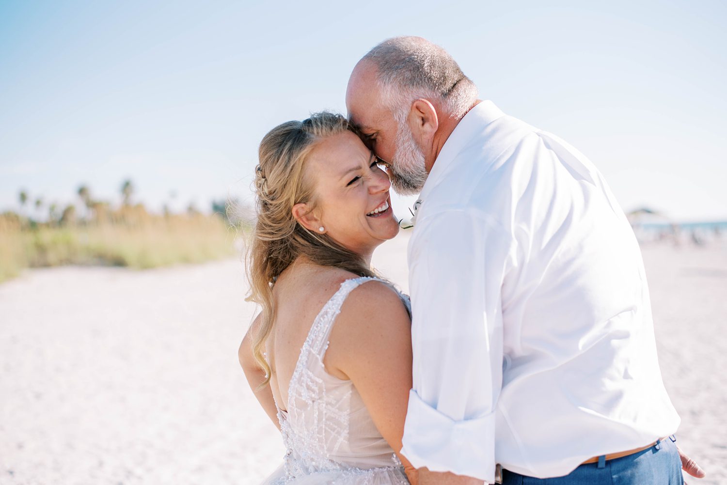 groom leans into bride's cheek making her laugh on beach wedding day