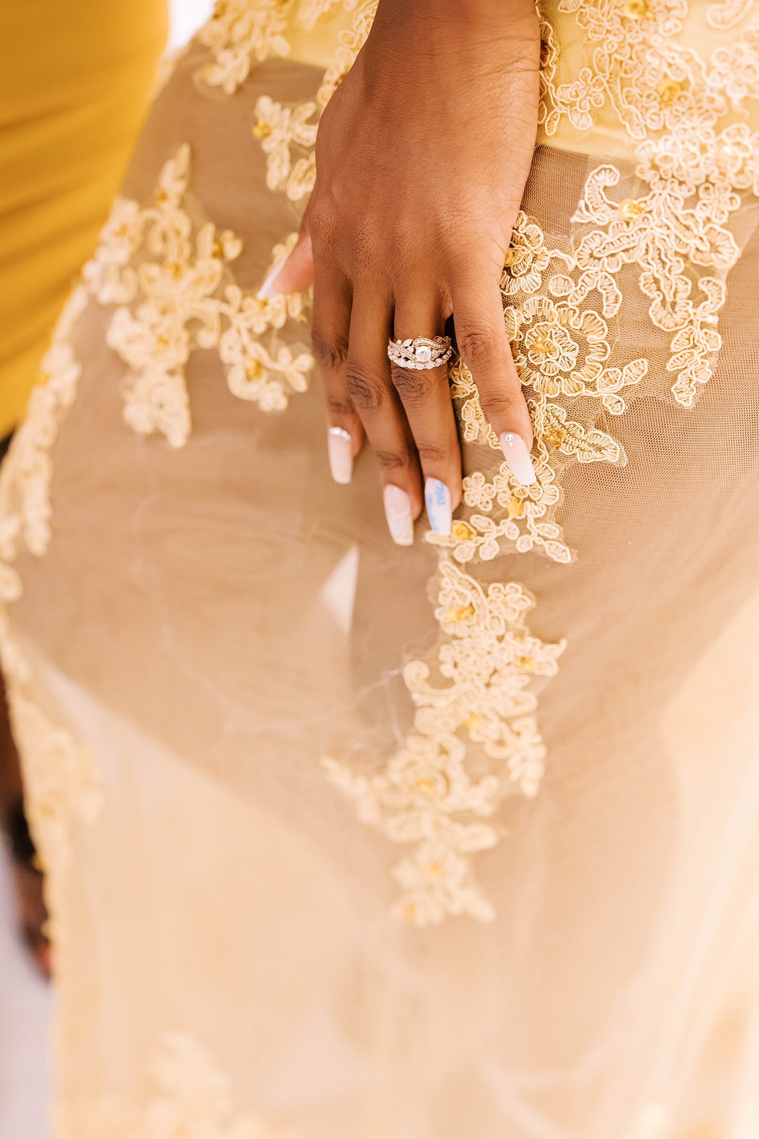 bride's hand with diamond ring rests against gold wedding gown with lace detail 
