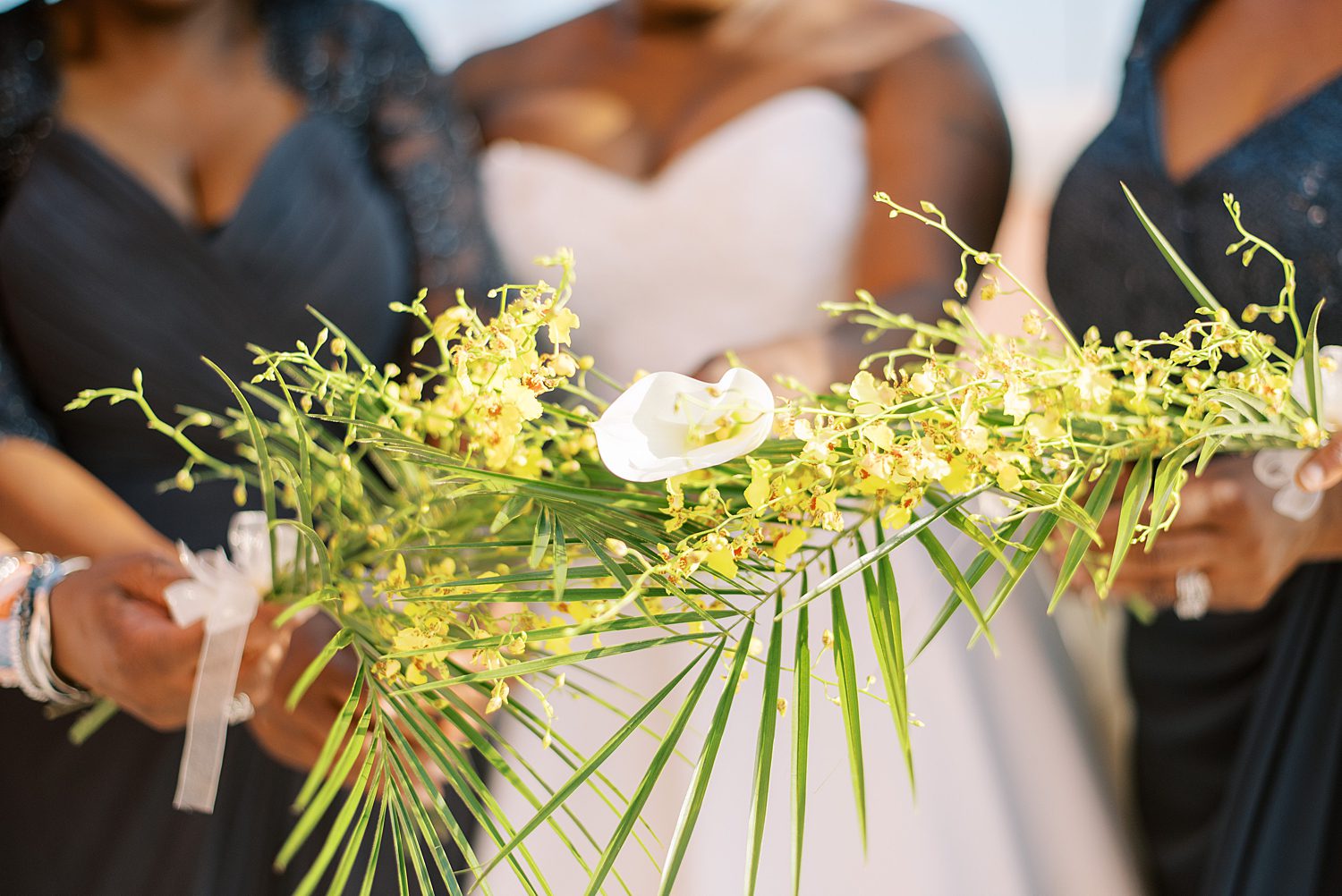 bride holds calla lily with  bridesmaids holding yellow tropical flowers