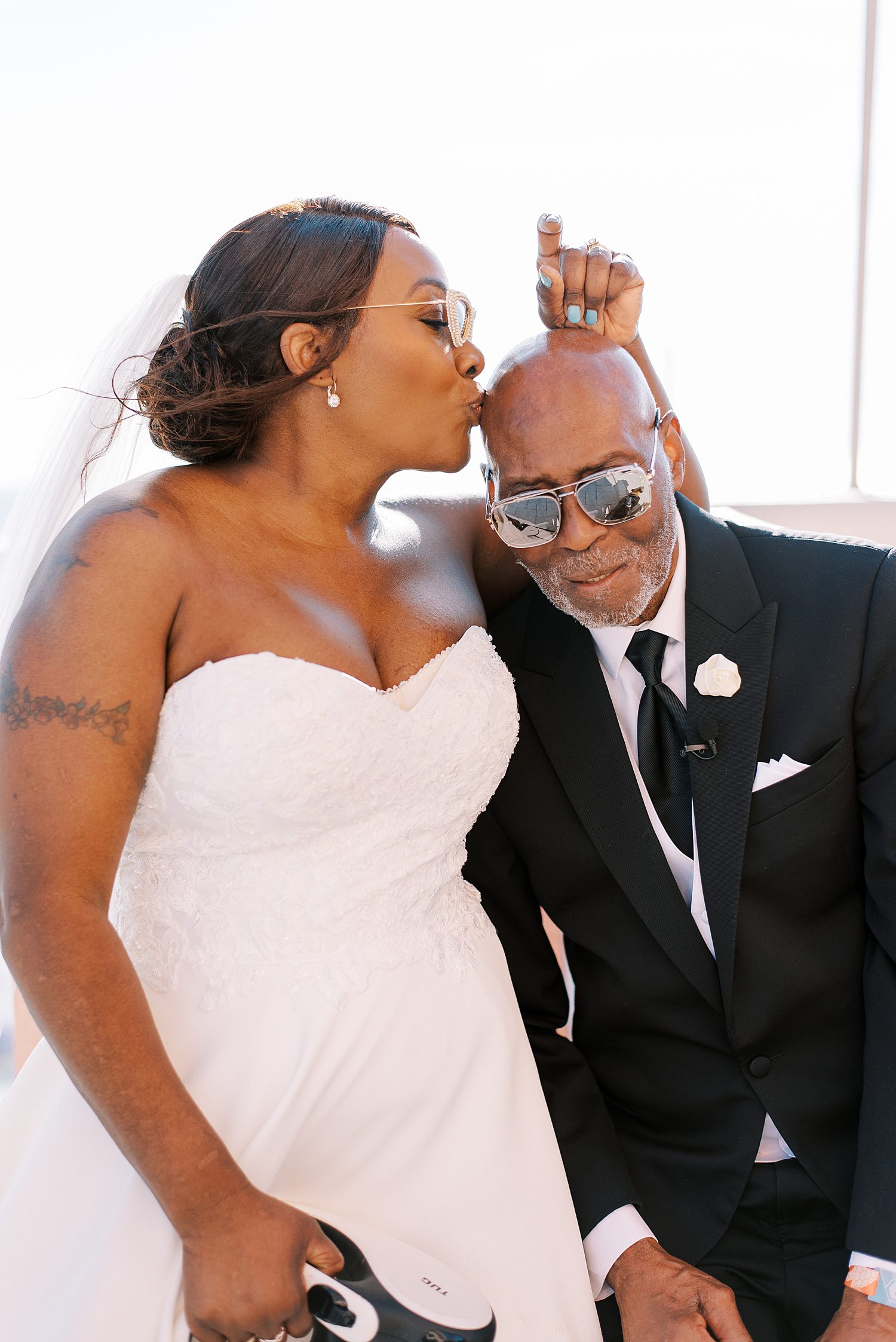 bride kisses groom's head during wedding portraits on patio