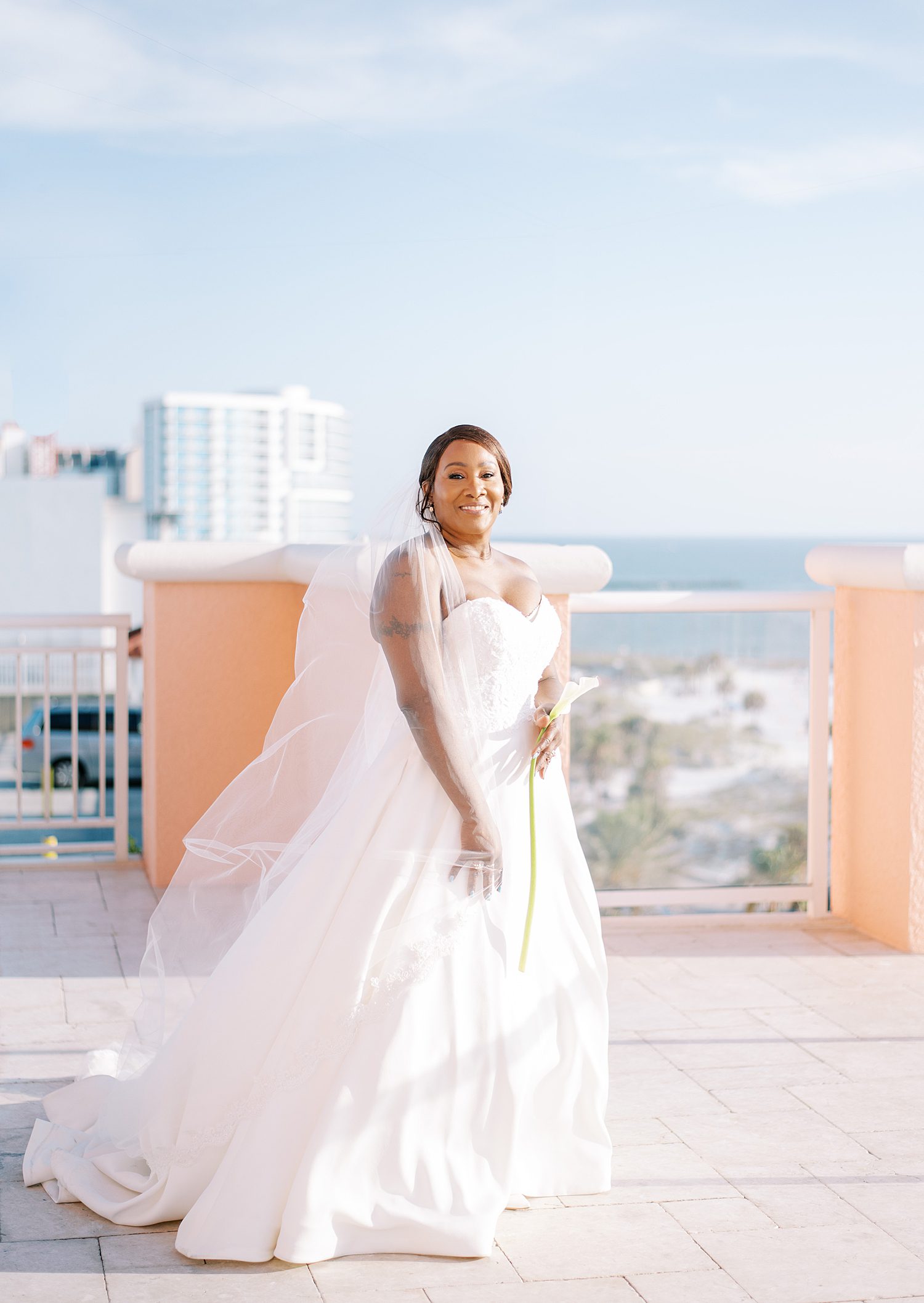 bride stands on balcony overlooking Tampa in strapless wedding gown