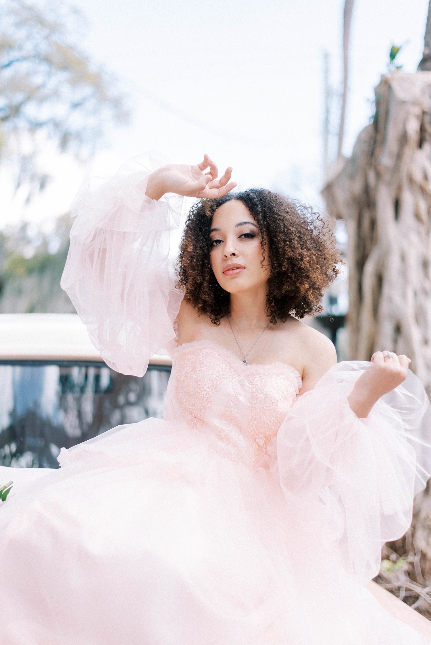 woman sits in pink dress with hand on forehead outside The Orlo