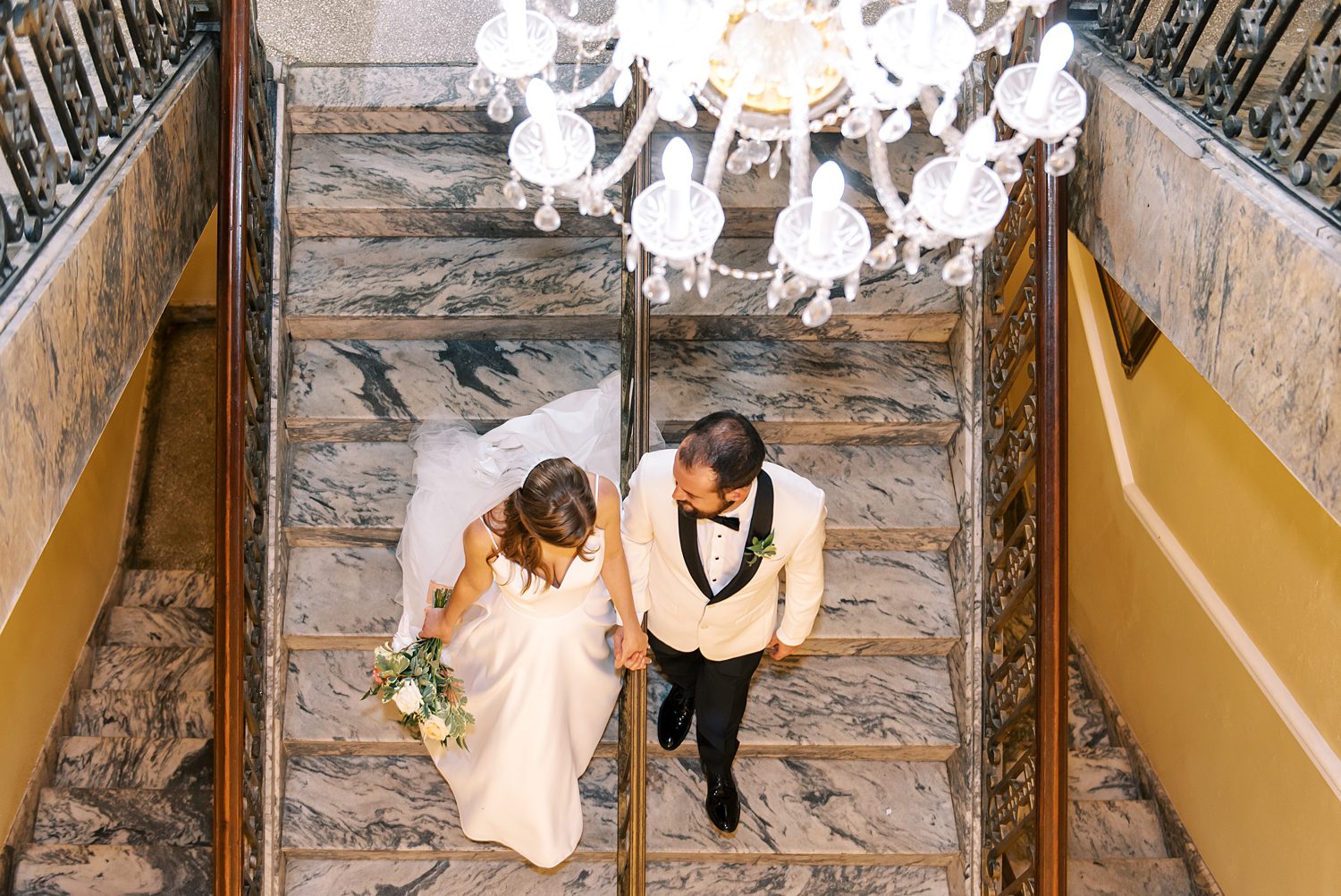 bride and groom hold hands walking down marble steps inside Centro Asturiano de Tampa