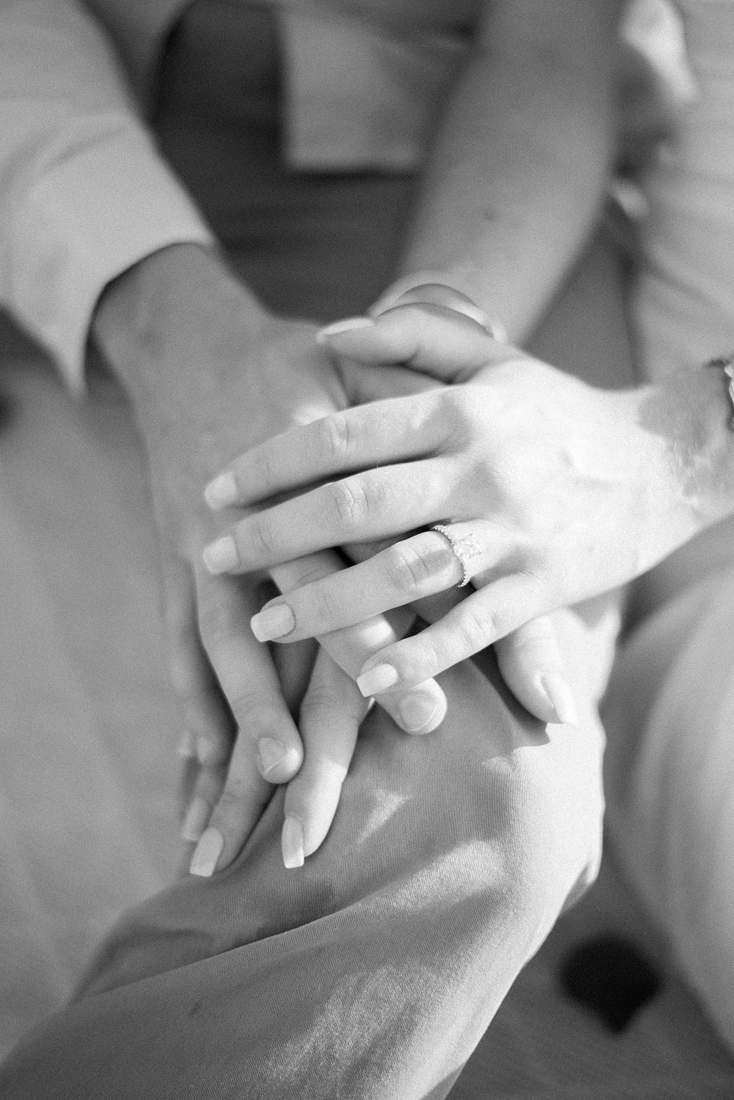 couple holds hands on man's knee showing off engagement ring