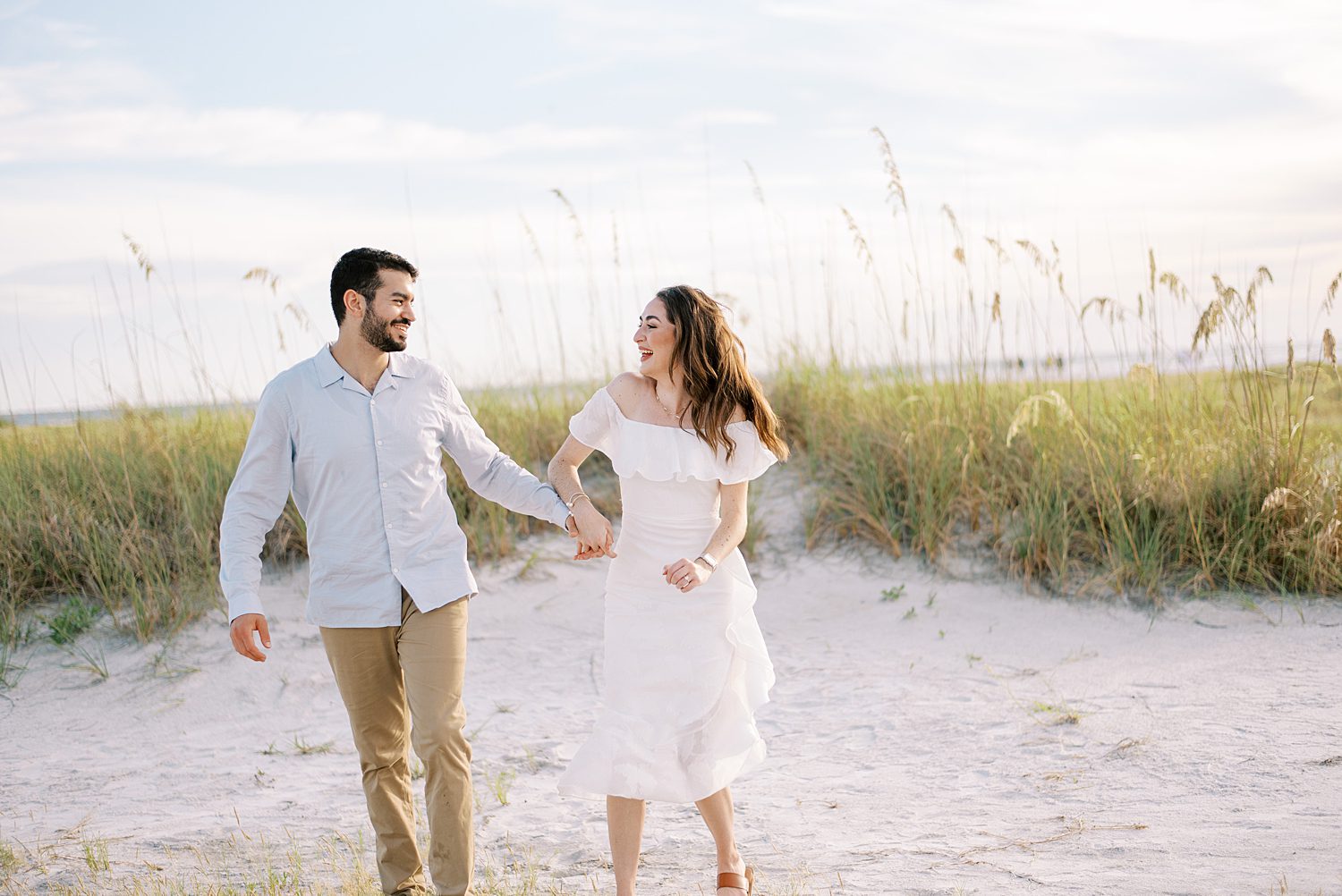 woman in off-the-shoulder white dress holds hands with man walking on Fort De Soto beach