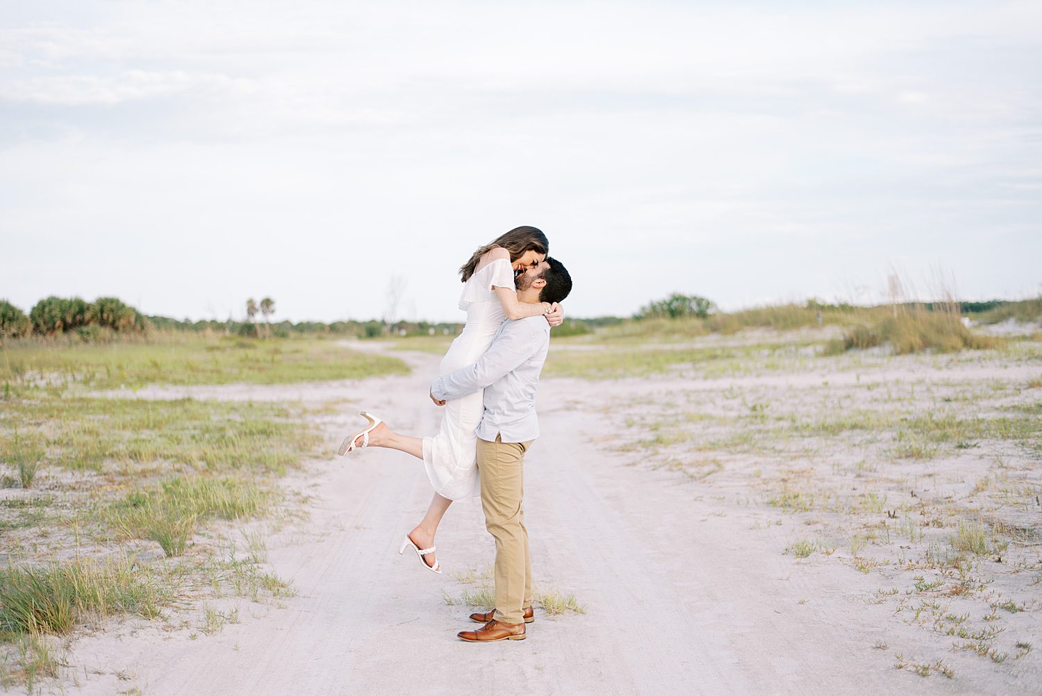 man lifts woman in white dress on path at Fort De Soto beach in Tampa FL