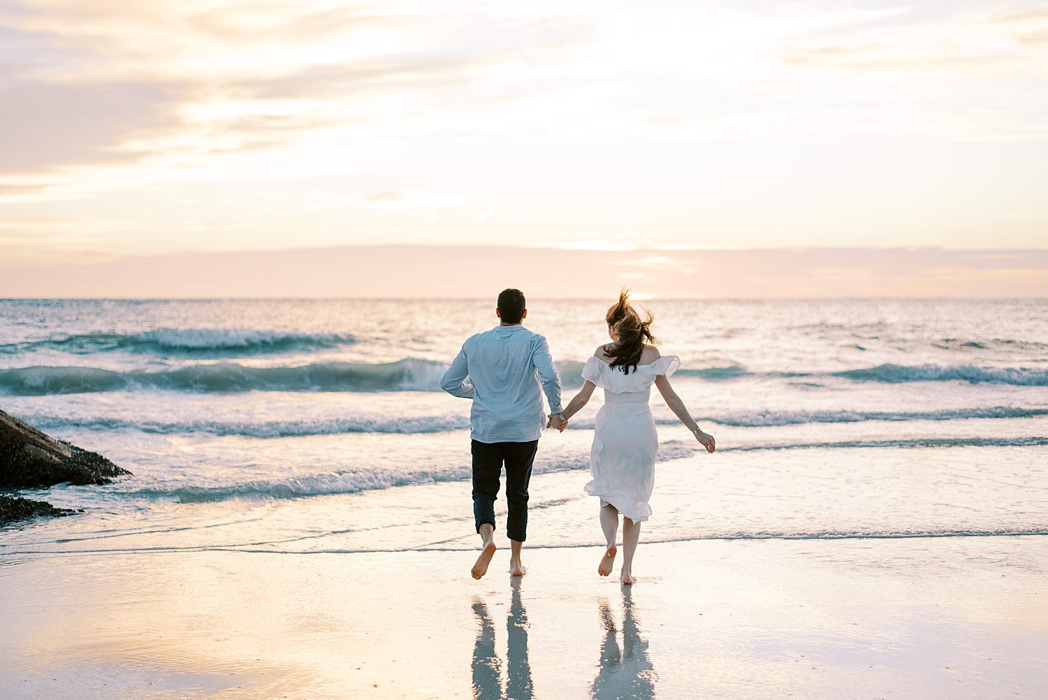 couple holds hands running towards ocean at Fort De Soto beach
