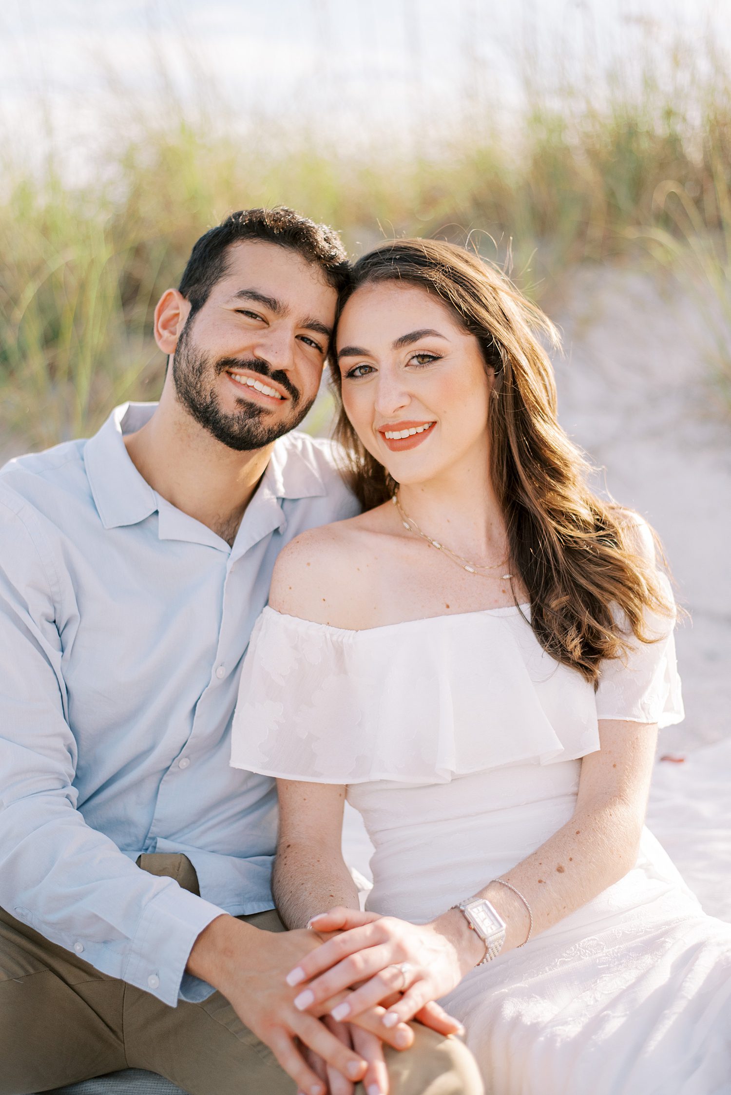 couple sits on dune at Fort De Soto beach leaning heads together