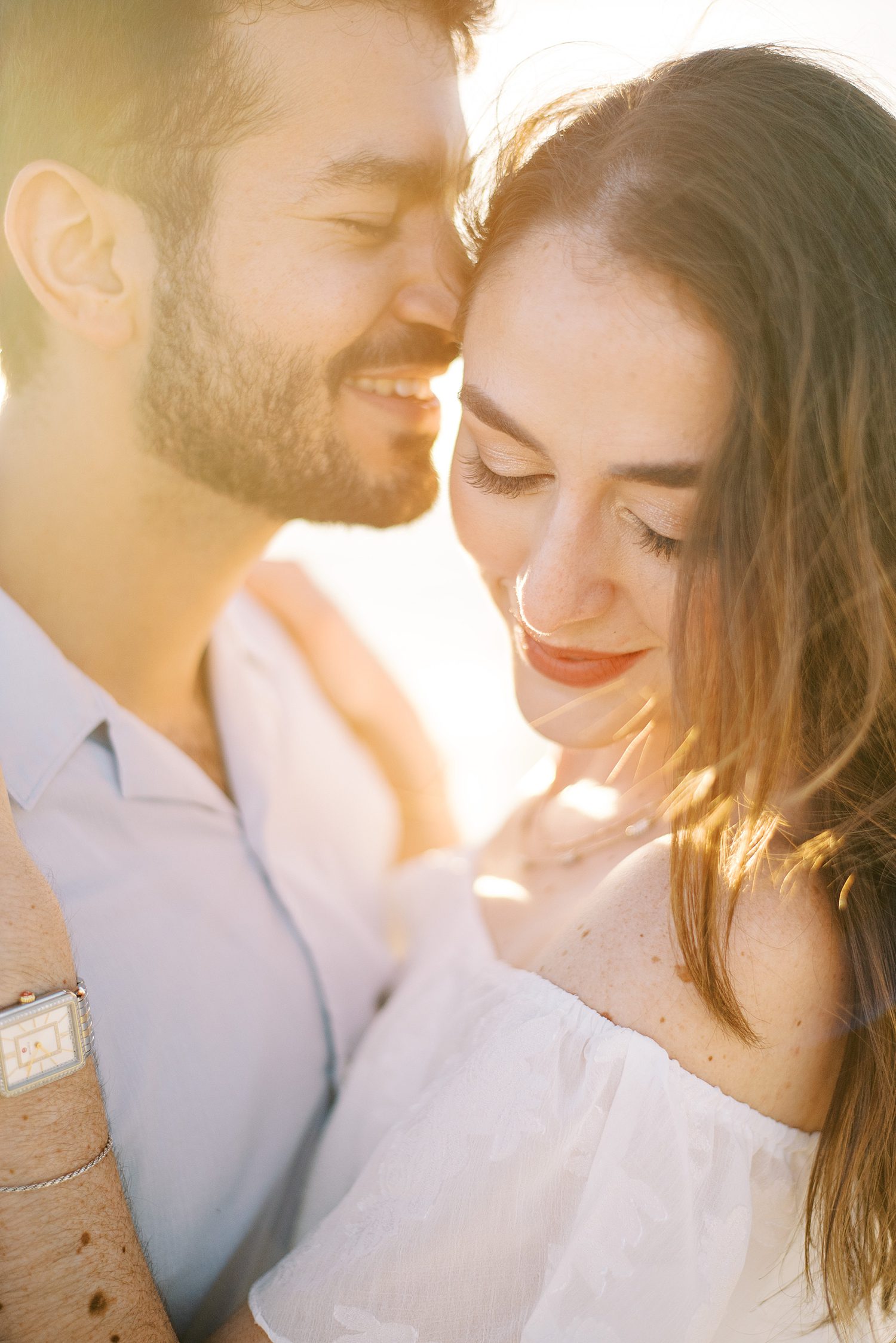 couple hugs while groom nuzzles woman's face at sunset