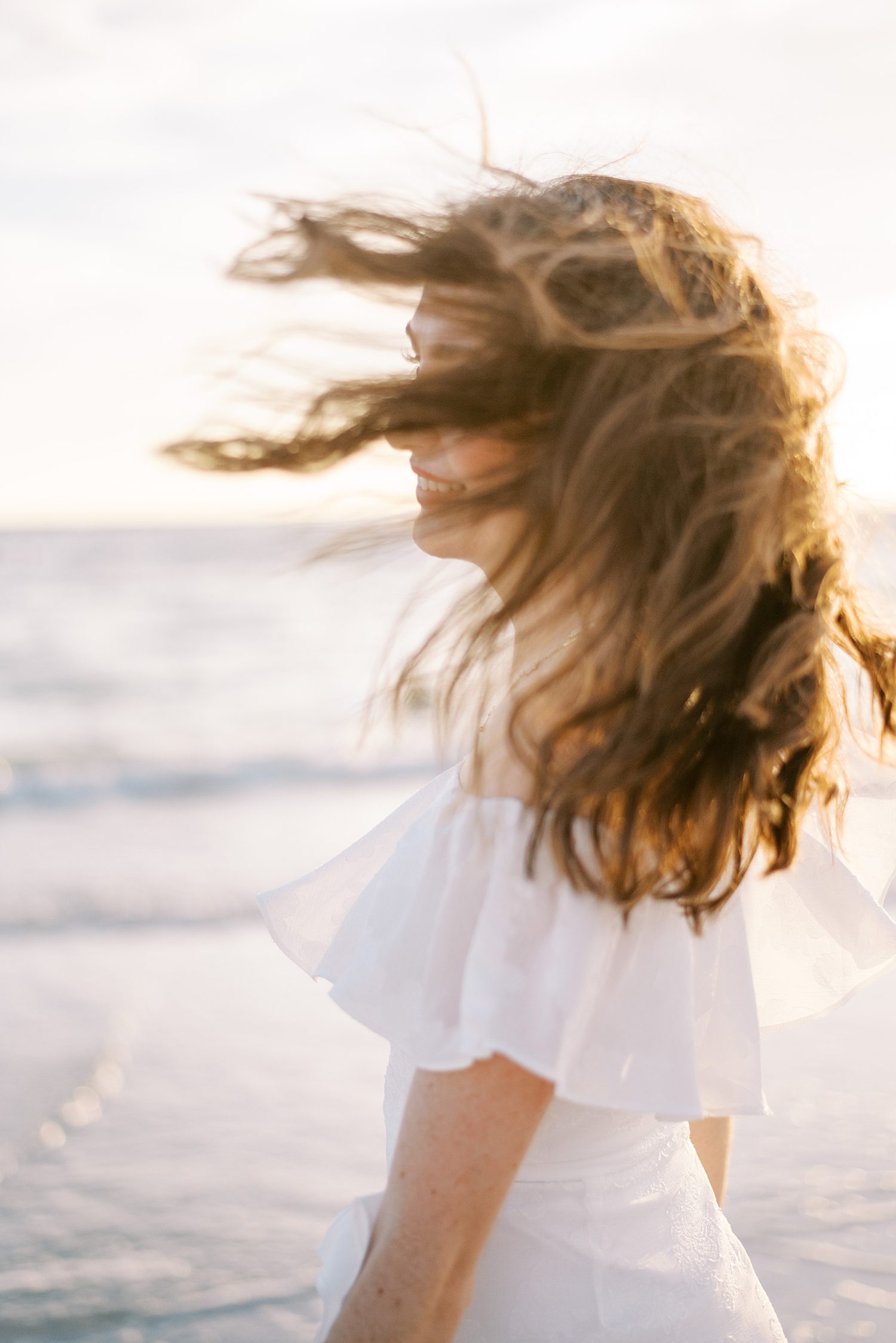 woman stands on beach with hair blowing in the wind