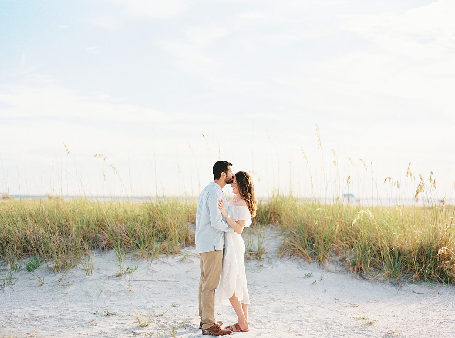 engaged couple hugs in front of Fort De Soto beach dunes