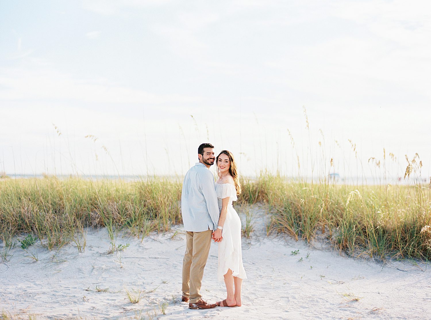couple holds hands in front of beach grass and dunes on Fort De Soto beach