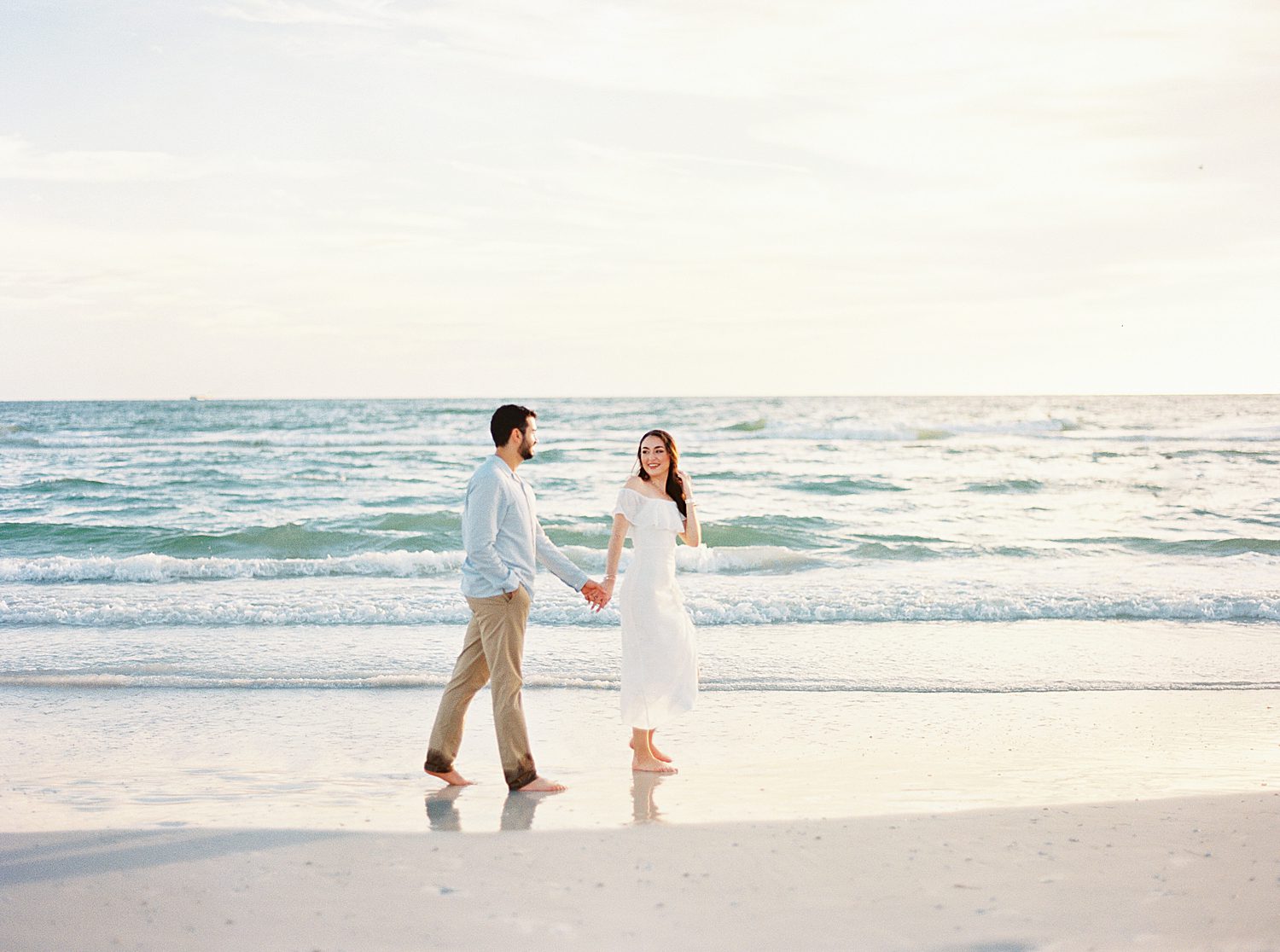 engaged couple holds hands walking by ocean on Fort De Soto beach