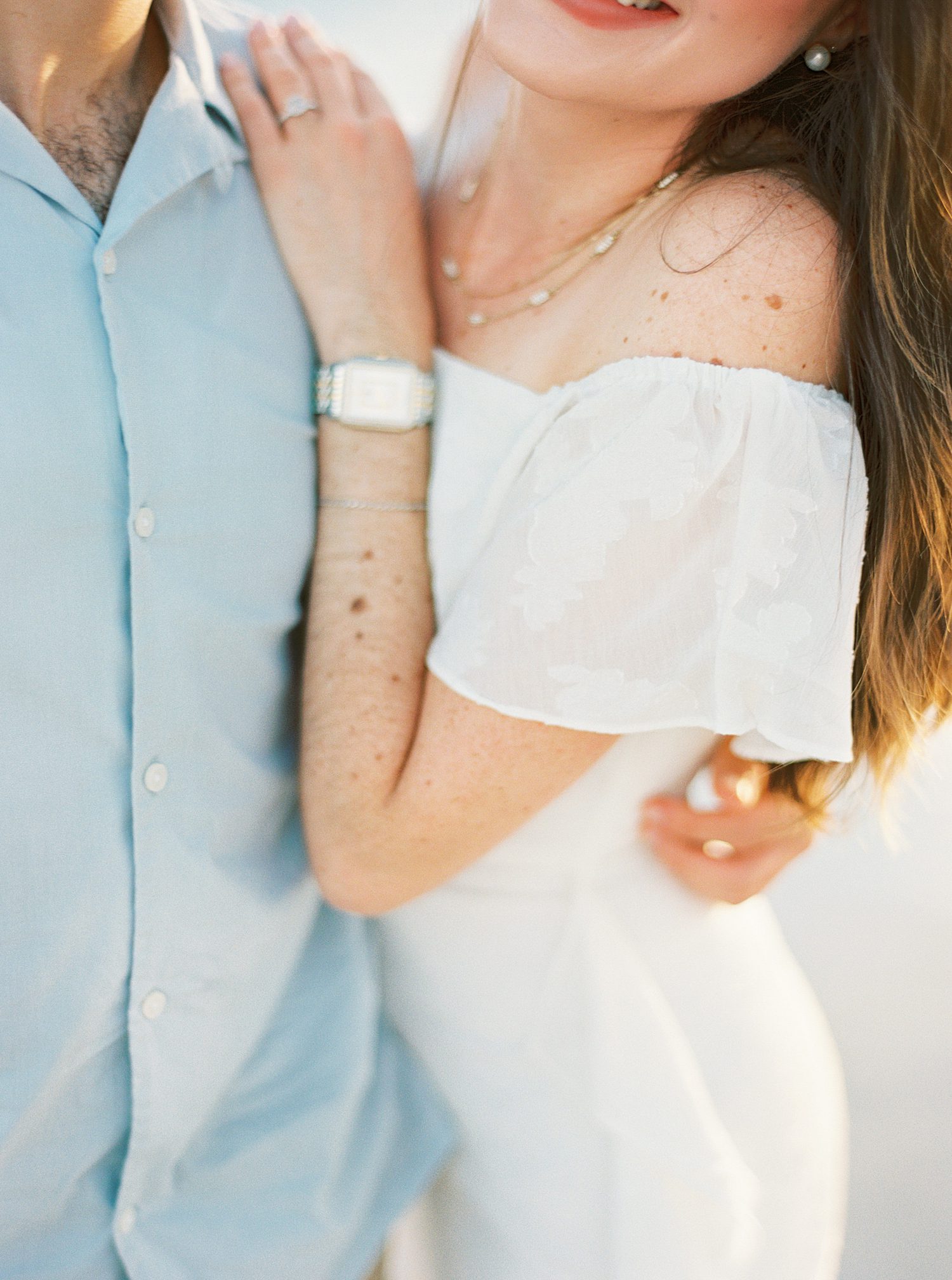 woman holds man's shoulder showing off watch and ring