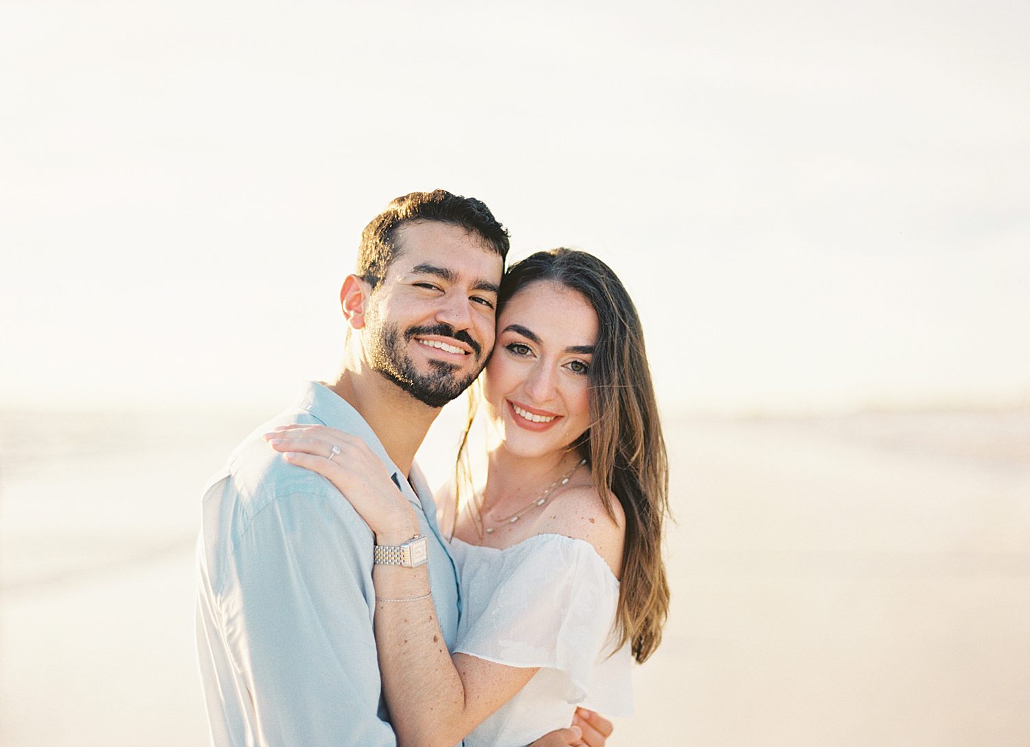 engaged couple hugs leaning heads together on beach