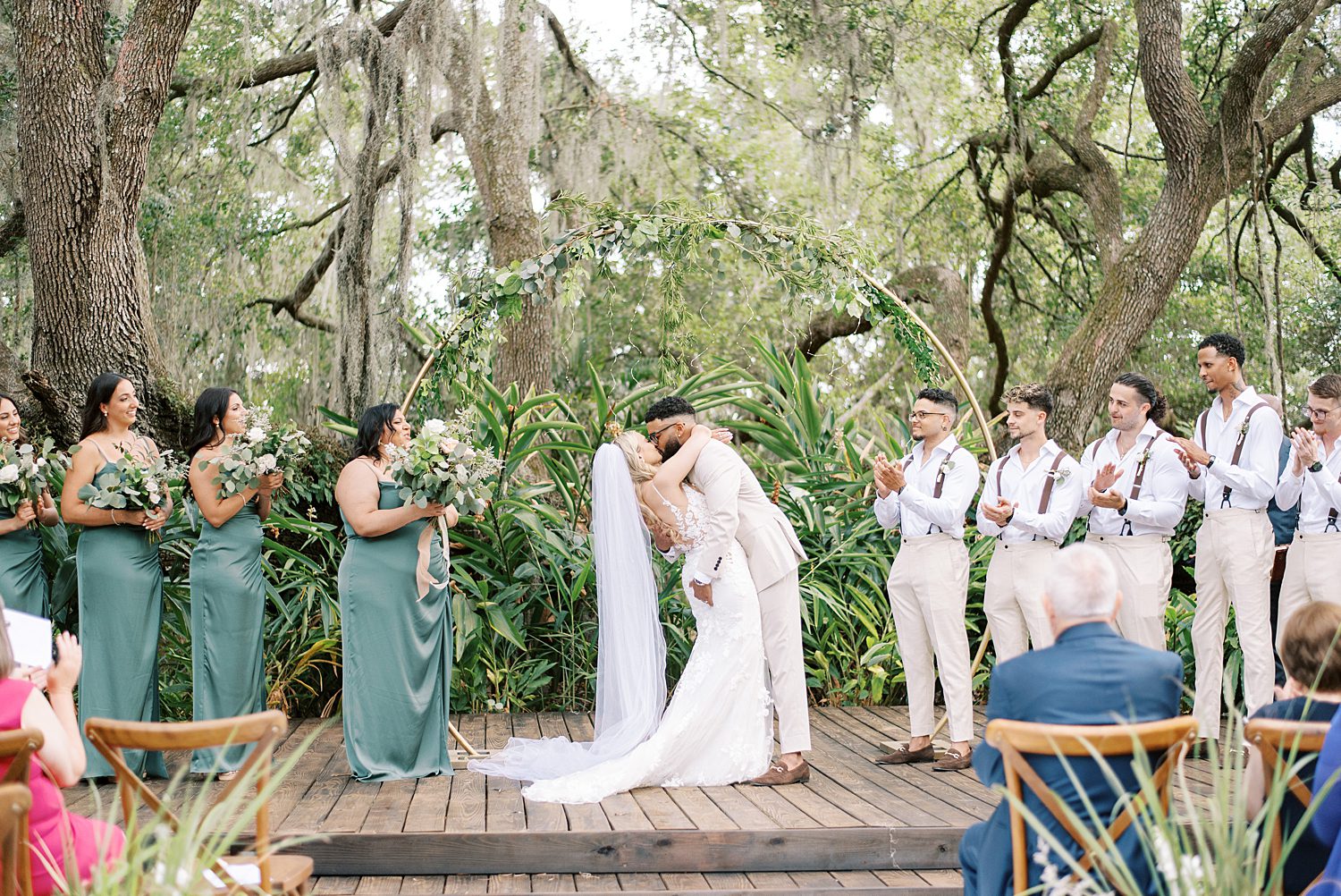 bride and groom kiss during ceremony under large oak tree at Mill Pond Estate