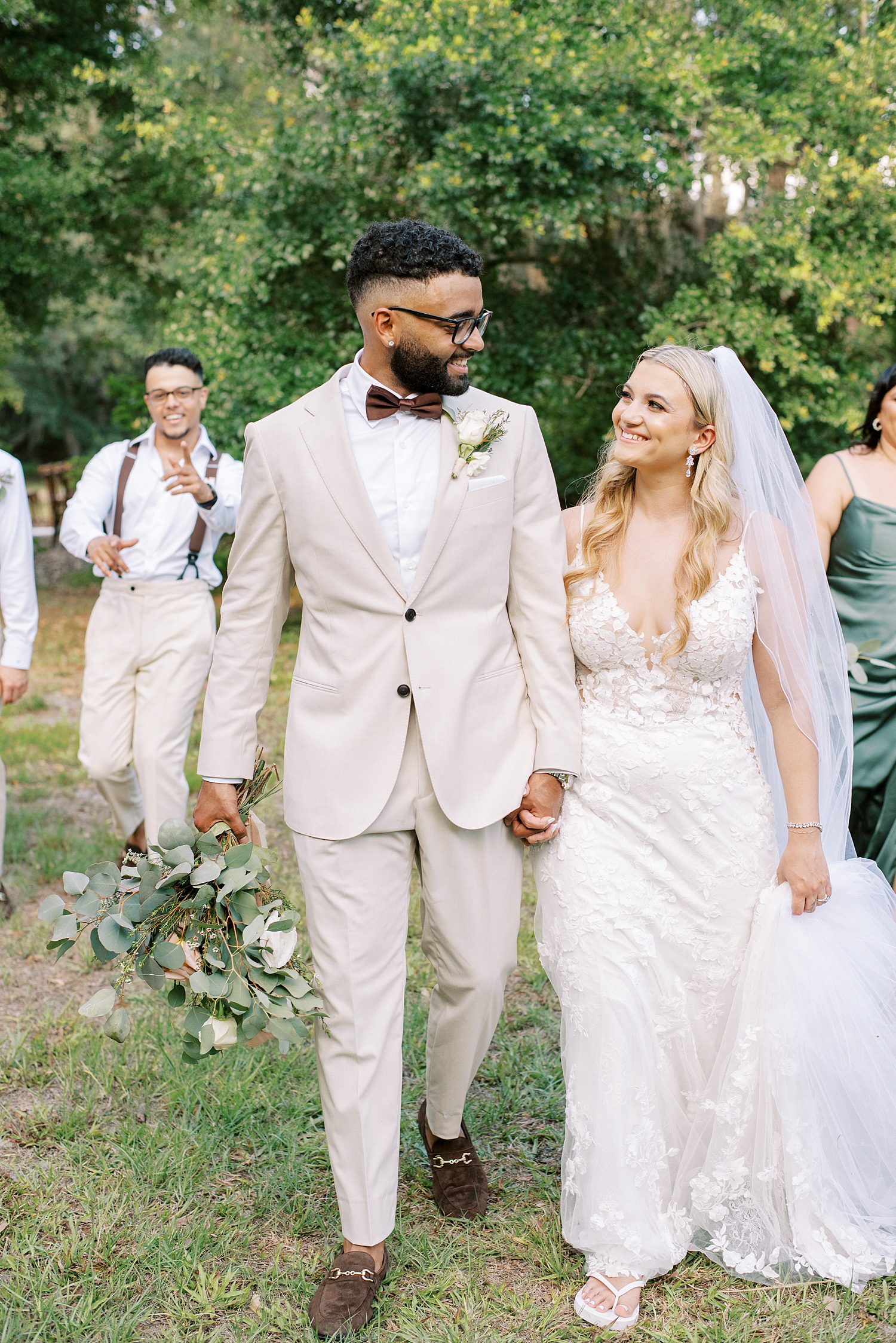 bride and groom hold hands walking in front of bridal party in tan and teal