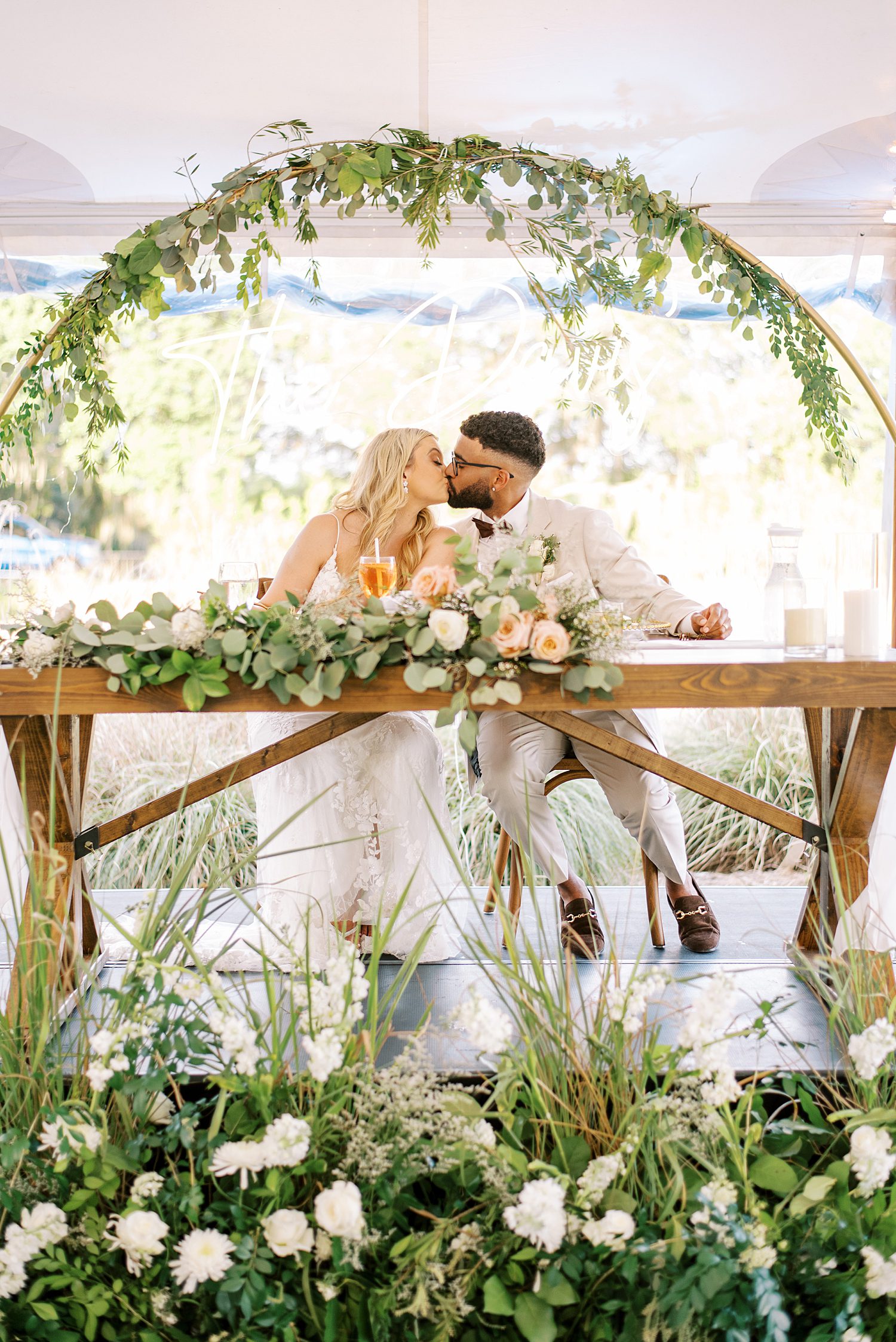 newlyweds kiss under arbor at Mill Pond Estate with white flowers 